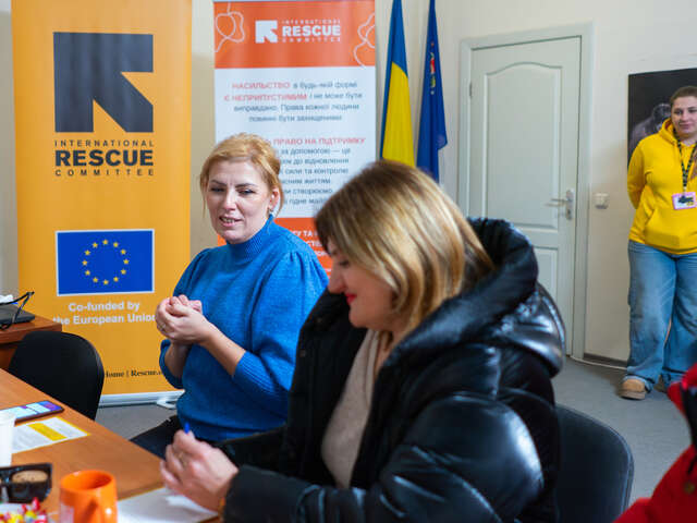 Zwei Frauen in der Ukraine sitzen an einem Tisch. Hinter ihnen ist das Logo von IRC.