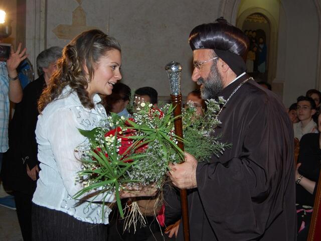 Mariela Shaker, with flowers, greets Syriac-Orthodox archbishop Mar Gregorios Yohanna Ibrahim.