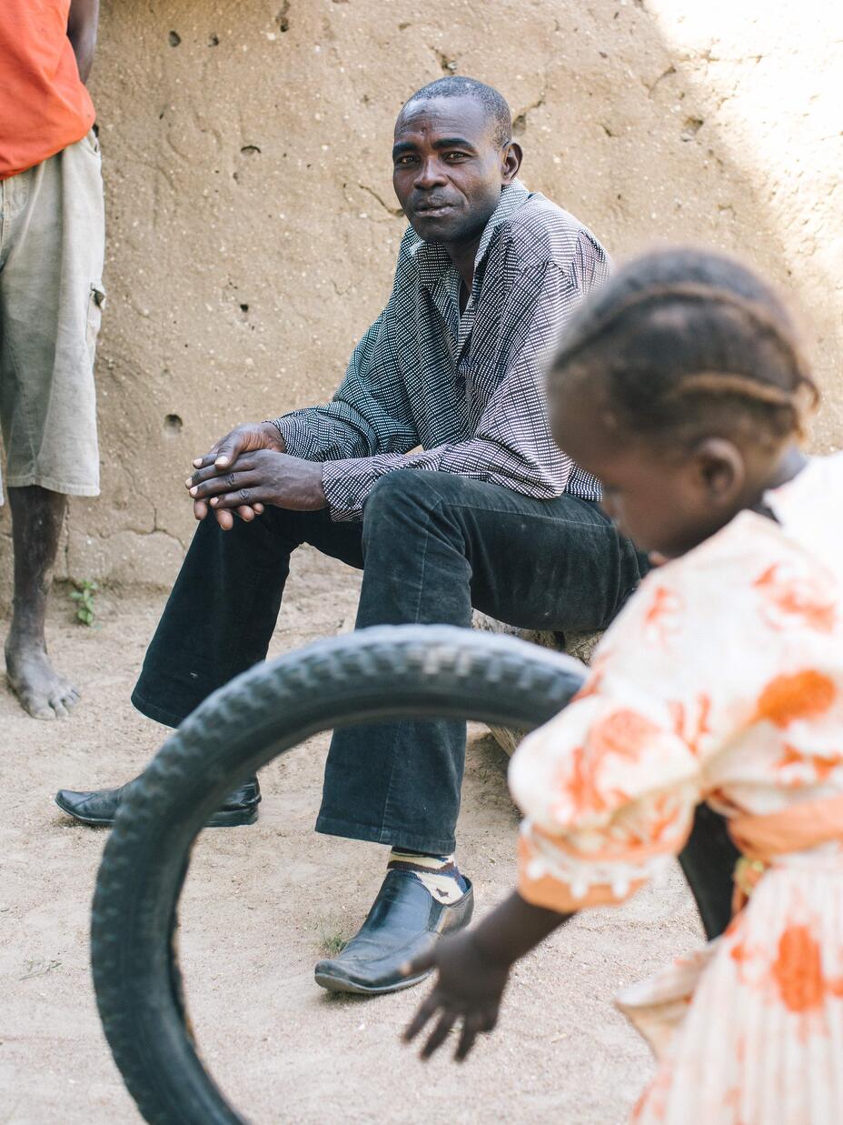 Simon sitting and his child playing with an old tire