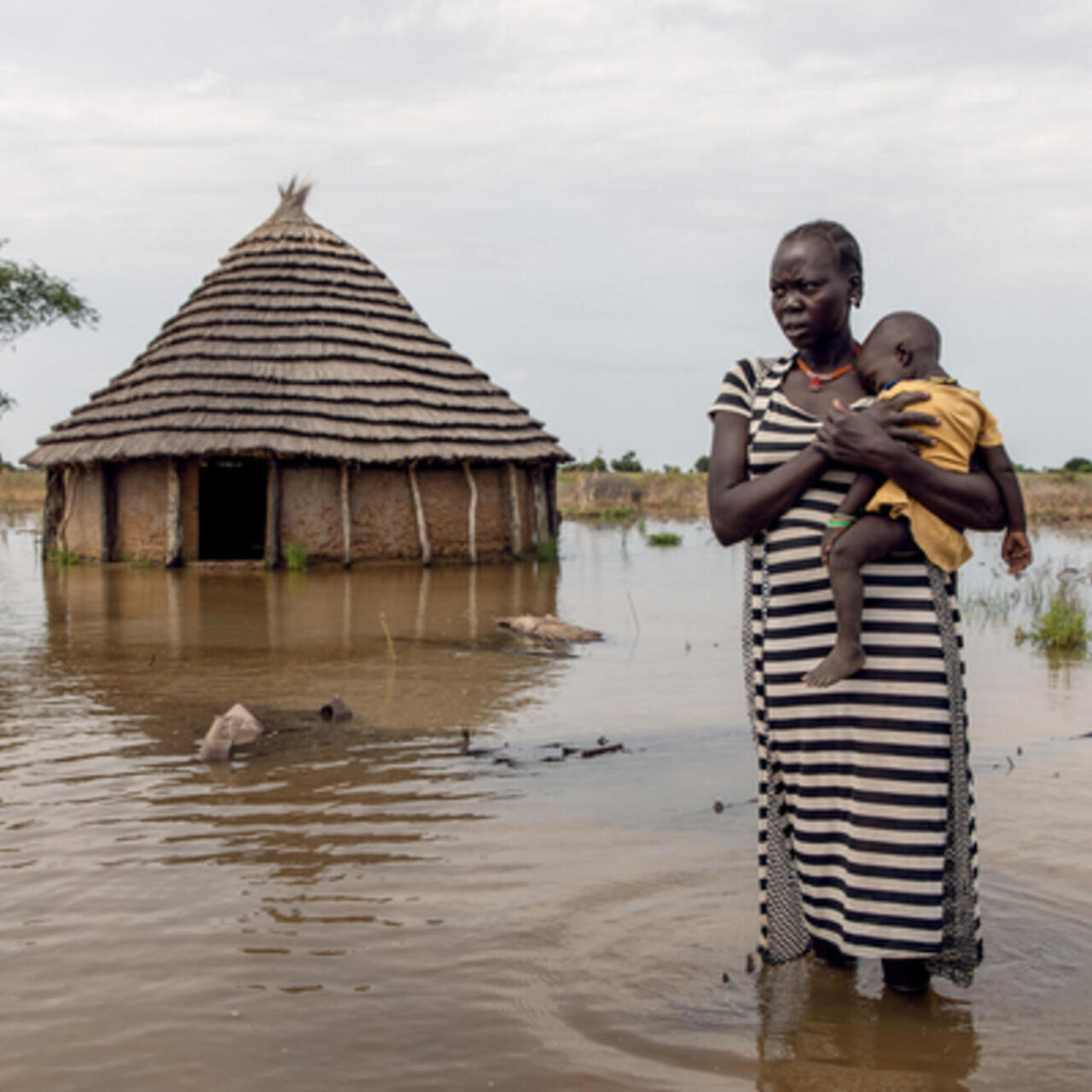 A mother carries her baby amidst flooding in South Sudan