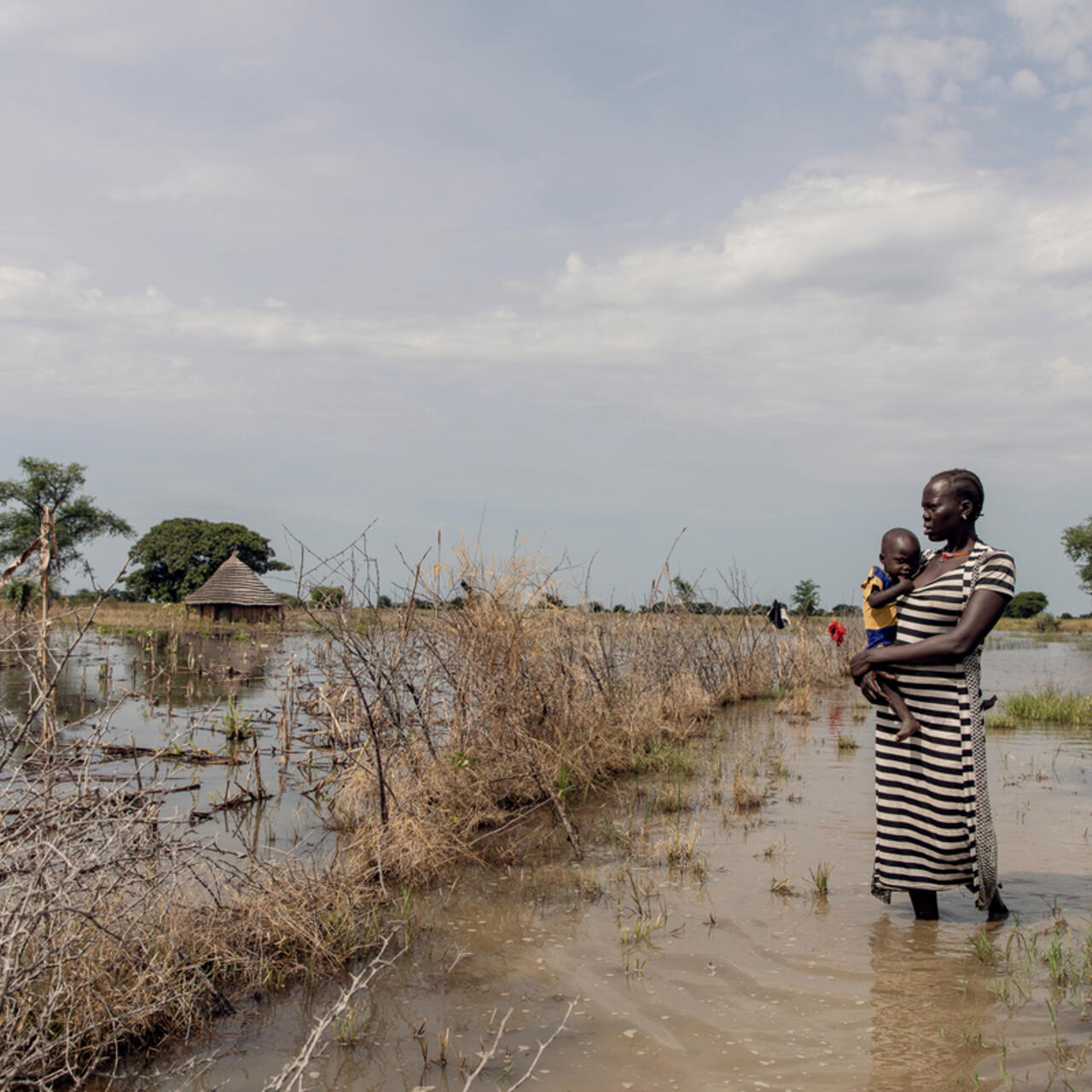 Abuk Deng holding her 4-year-old daughter Nyirou in front of their flooded home in Northern Bahr el Ghazal, South Sudan.