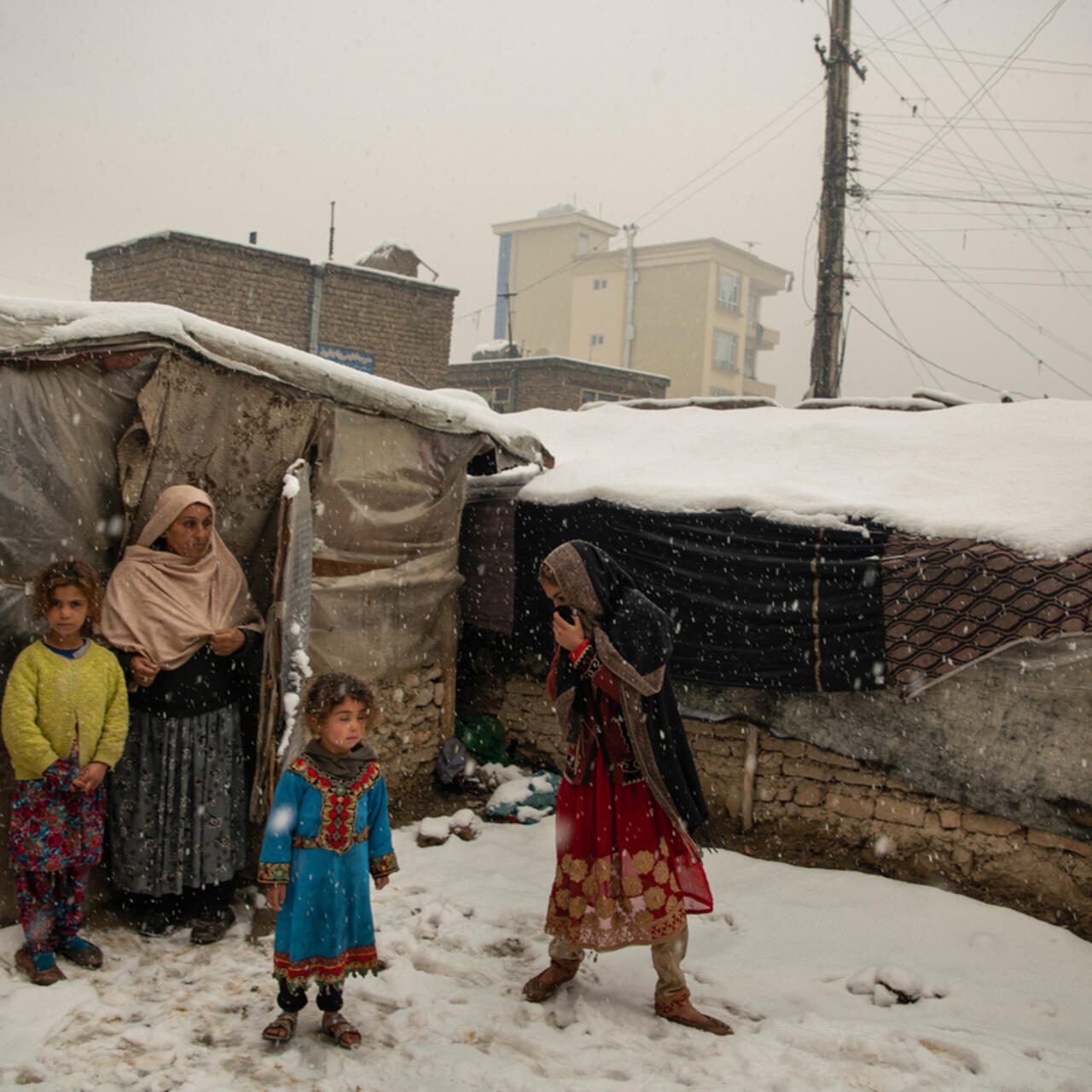 An Afghan family huddles in the snow outside their makeshift house