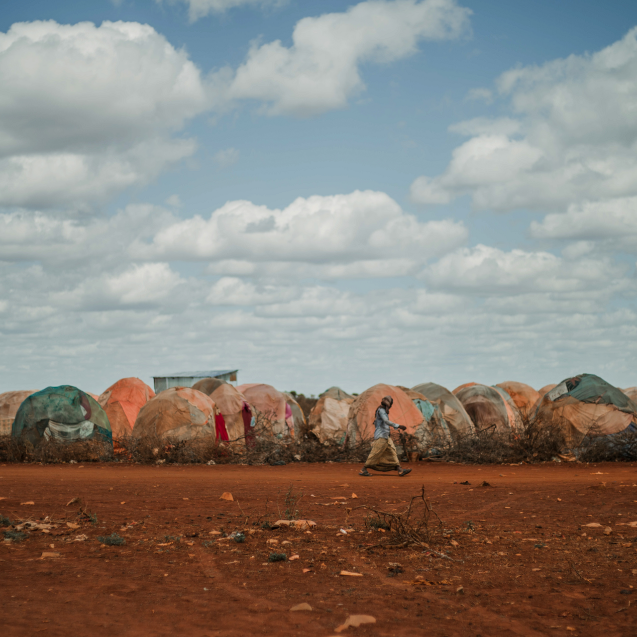 A wmen walks in front of a row of makeshift shelters in Somalia. The environment is barren and drought-stricken.