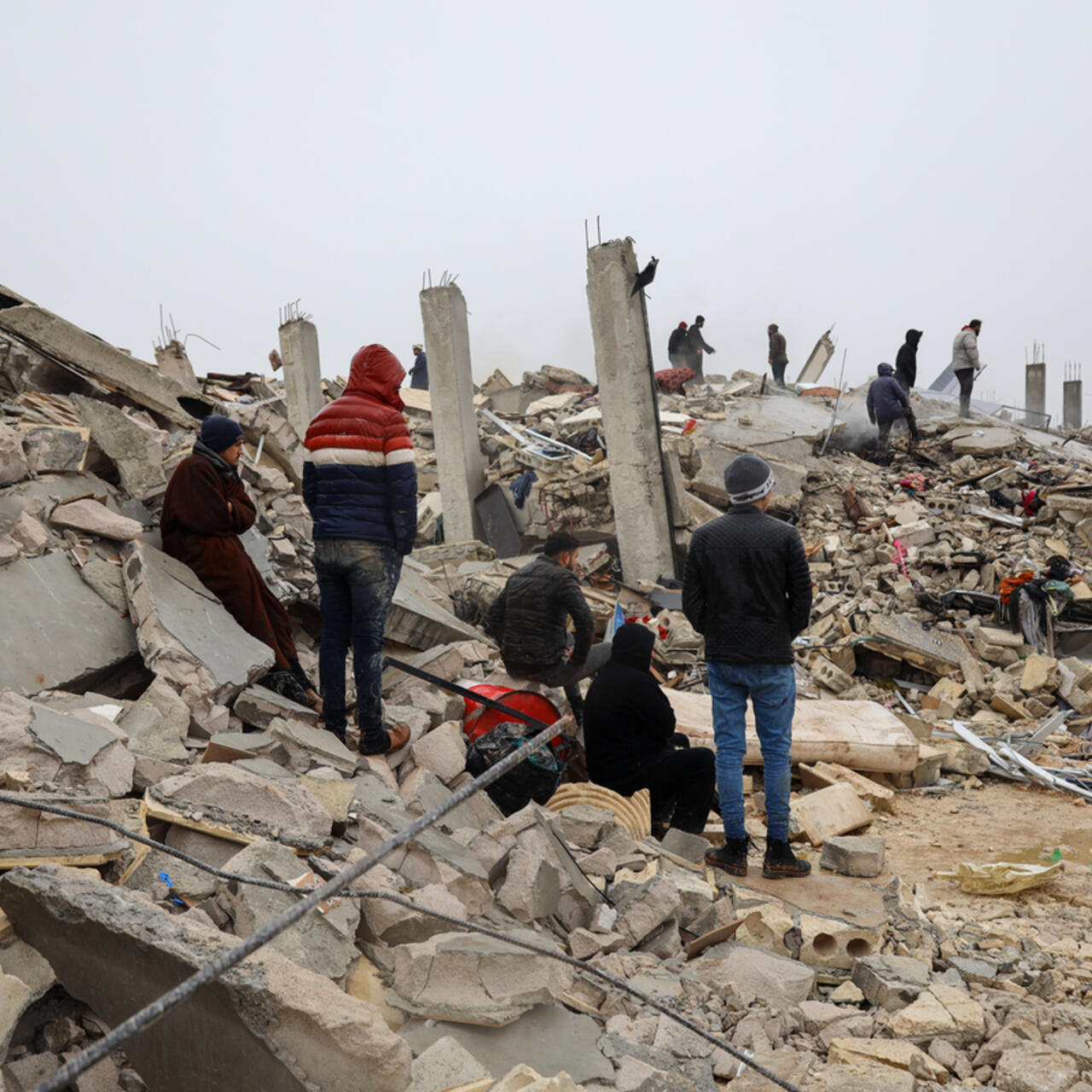 A group of survivors standing in rubble following the February 2023 earthquake in Syria.