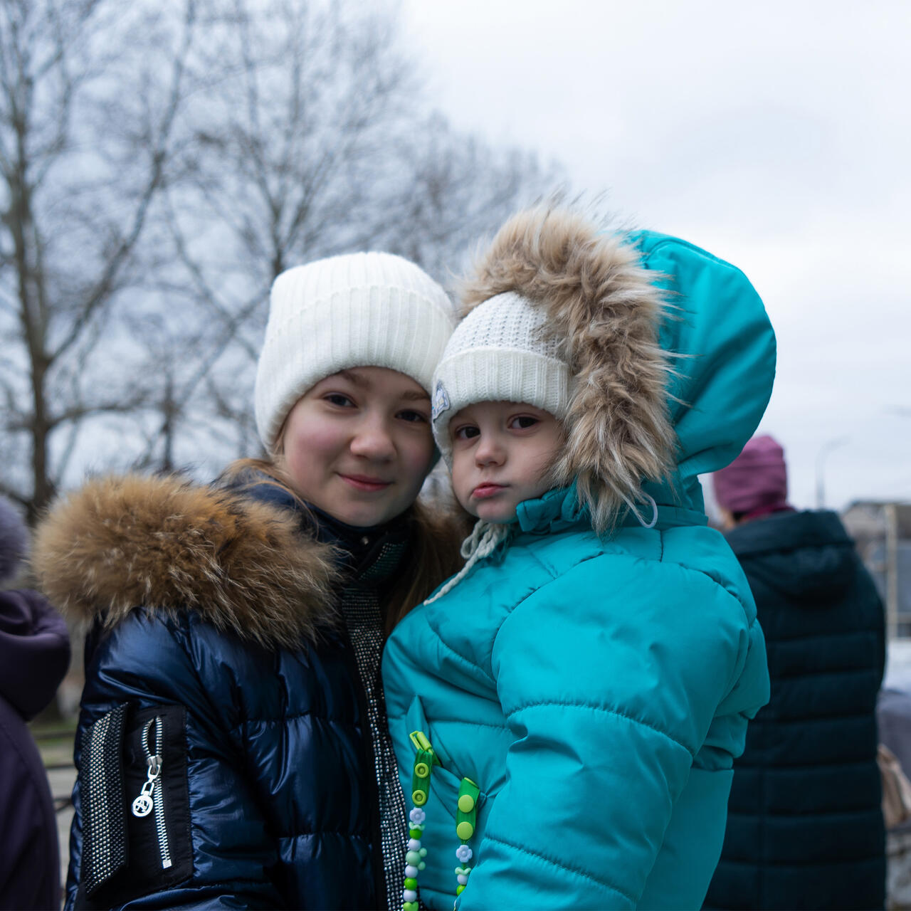 Two young girls outfitted in snow gear embrace. They are waiting for their parents to pick up their winter kits from the IRC in Ukraine.