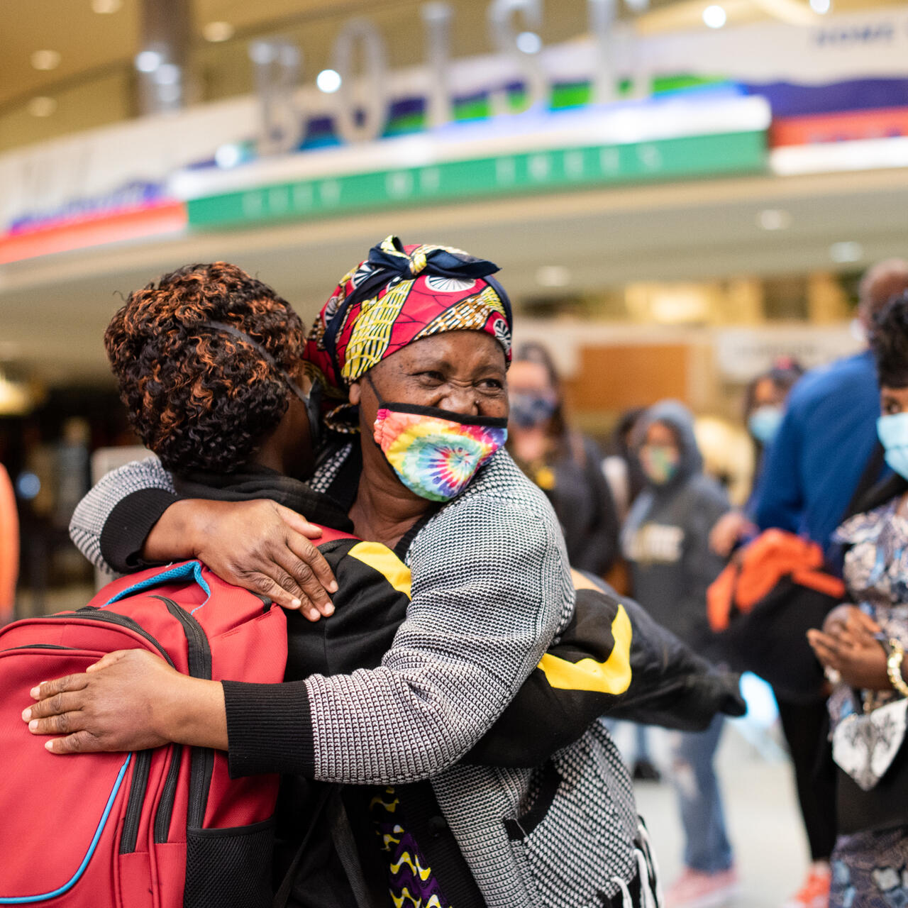 A refugee family is reunited at an American airport. The family hug each other in a warm embrace and smile.