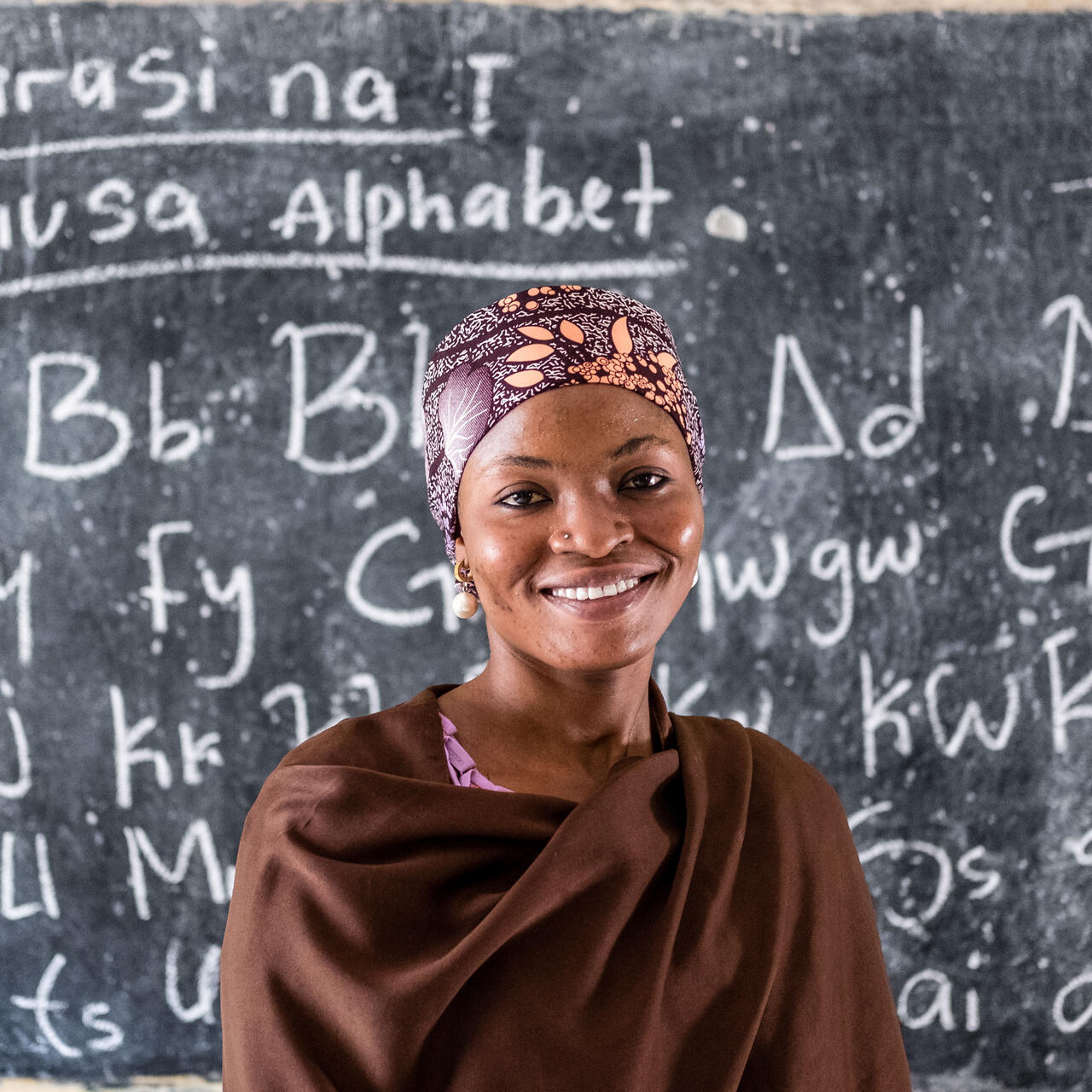 A girl stands in front of a school chalkboard.