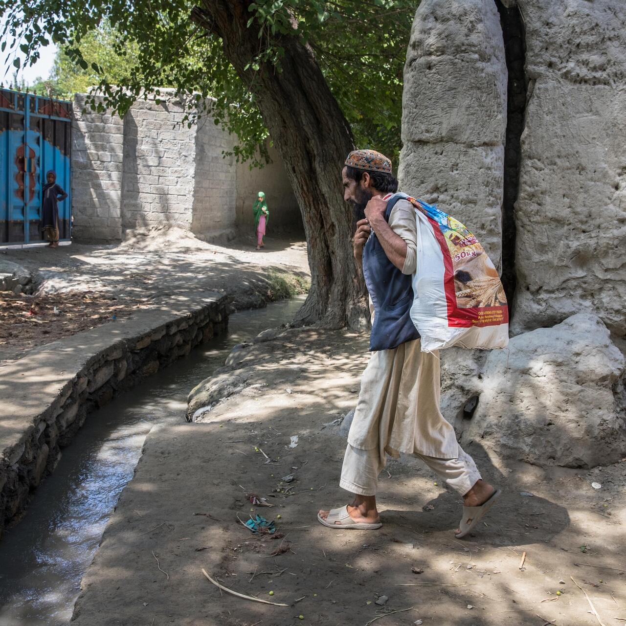 A man walks with a sack over his back, filled with pickles to sell at the bazar.