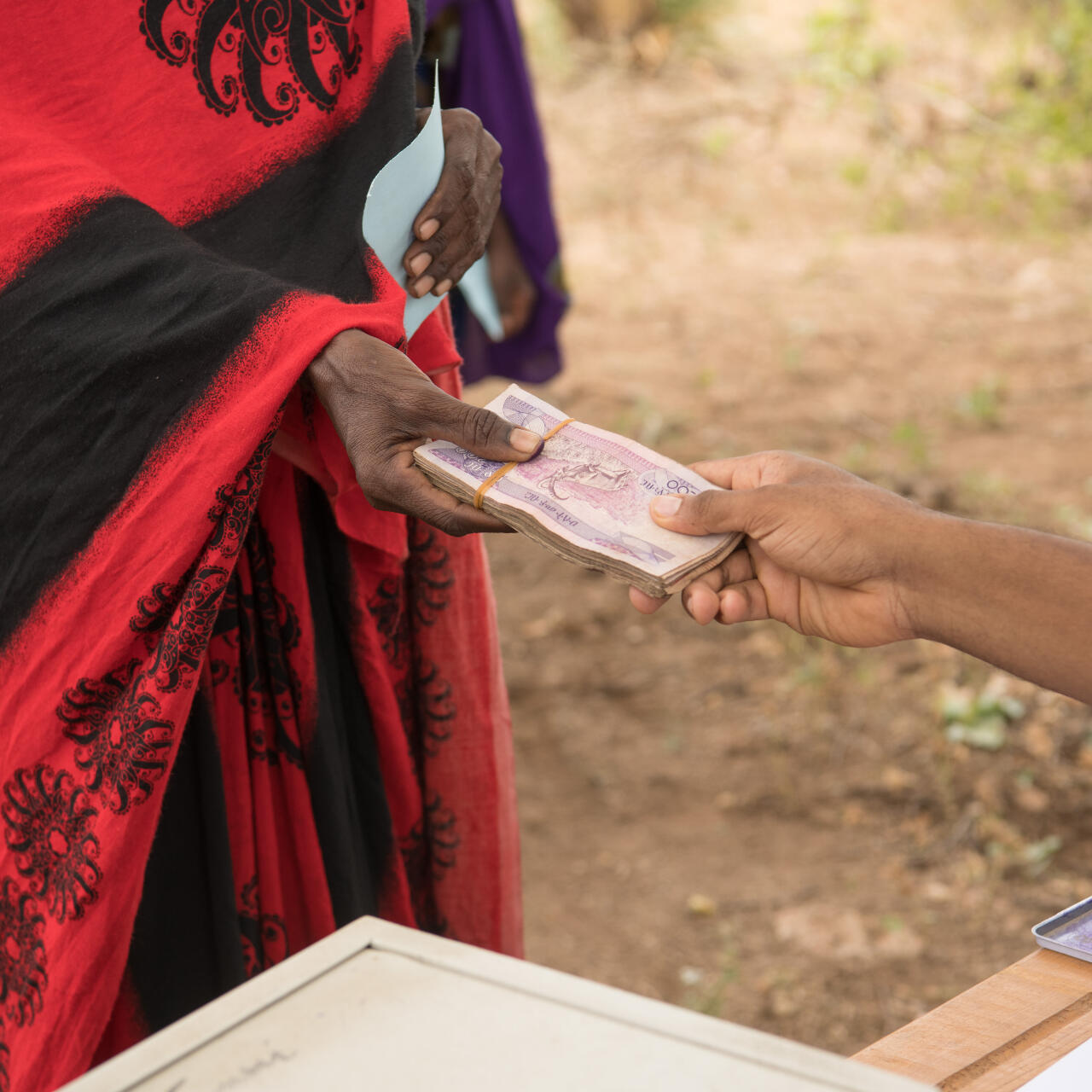 Two people exchange a stack of Ethiopian currency. The bills are pink in color.