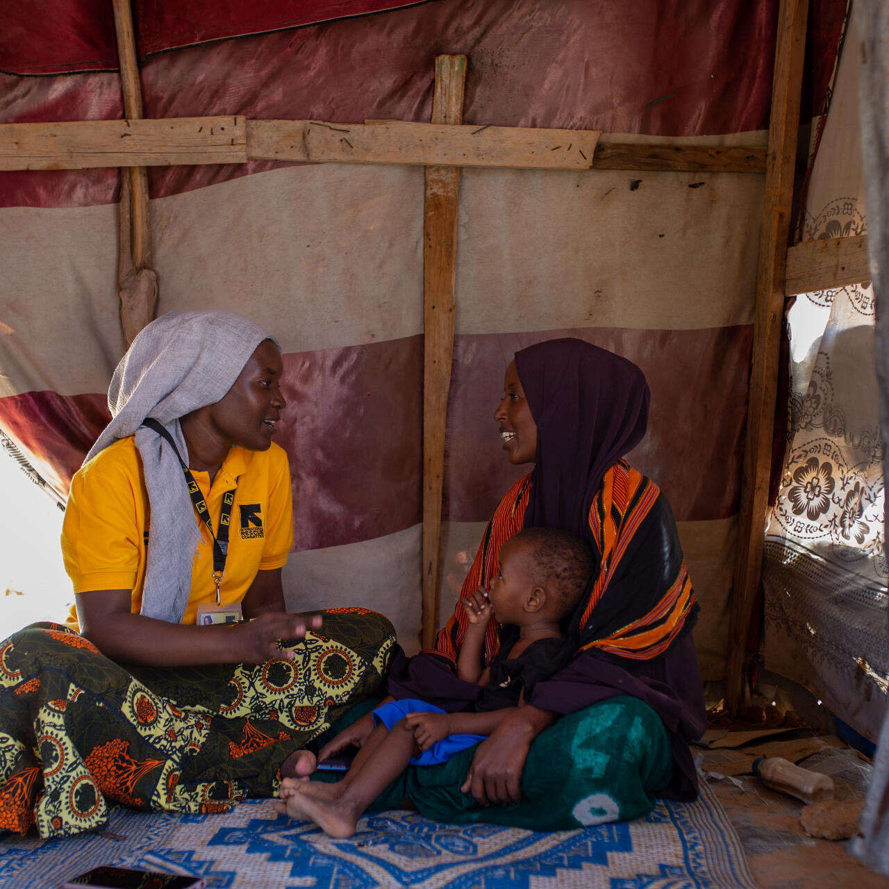 An IRC staff member consults a mother and her child inside a small building in a camp for internally displaced Somalis. The pair share a conversation while sitting on the floor.