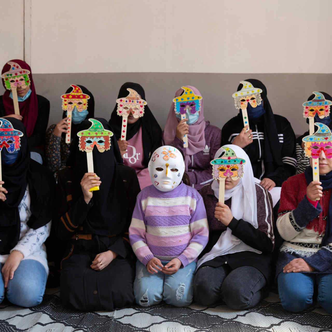 A group of young Syrian refugee girls wearing masks they made during a drawing activity.