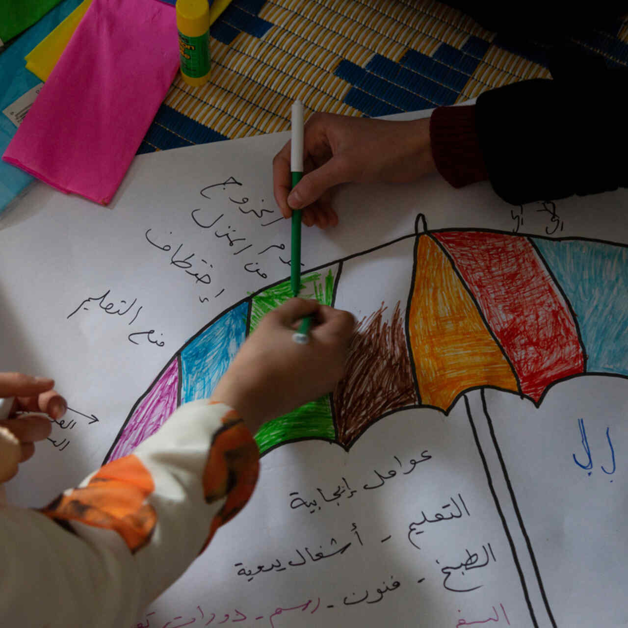 Syrian refugee girls color and write on a carton on the floor in the safe space where they take part in different kind of activities with the IRC WPE team.