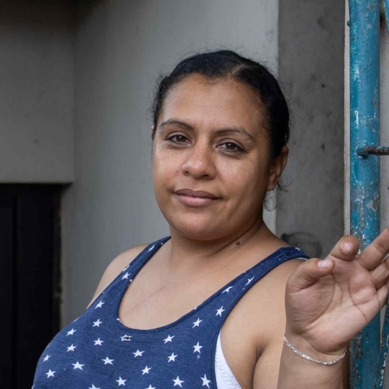 A Honduran woman poses for a portrait photo next to a blue gate.