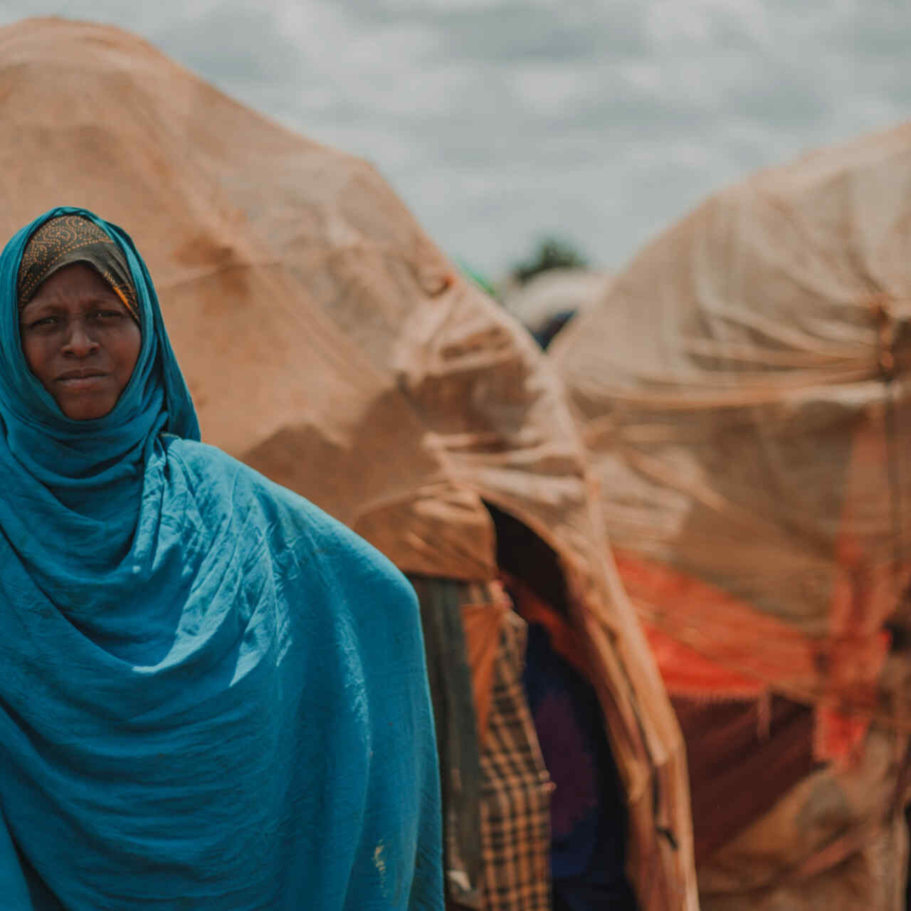 A woman poses for a photo outside of a small structure covered in blankets in Torotorow IDP Camp, Somalia.