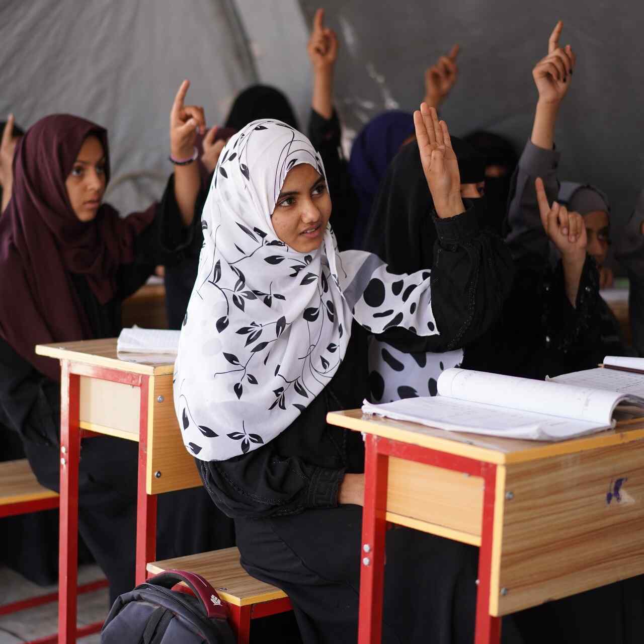 Photo of a classroom of girls in Yemen, raising their hands during a lecture. 