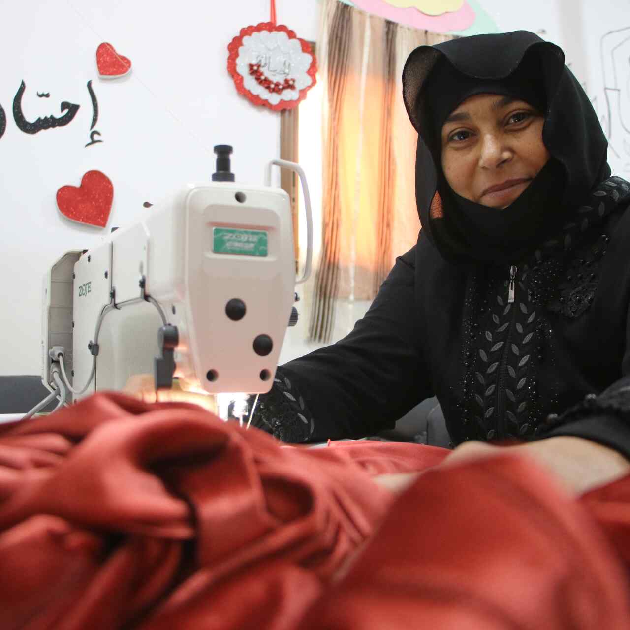 Mustafa sews a red piece of clothing.