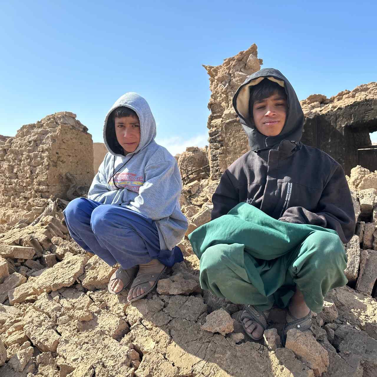 Two Afghan boys sit atop a pile of rubble from a building destroyed by an earthquake.