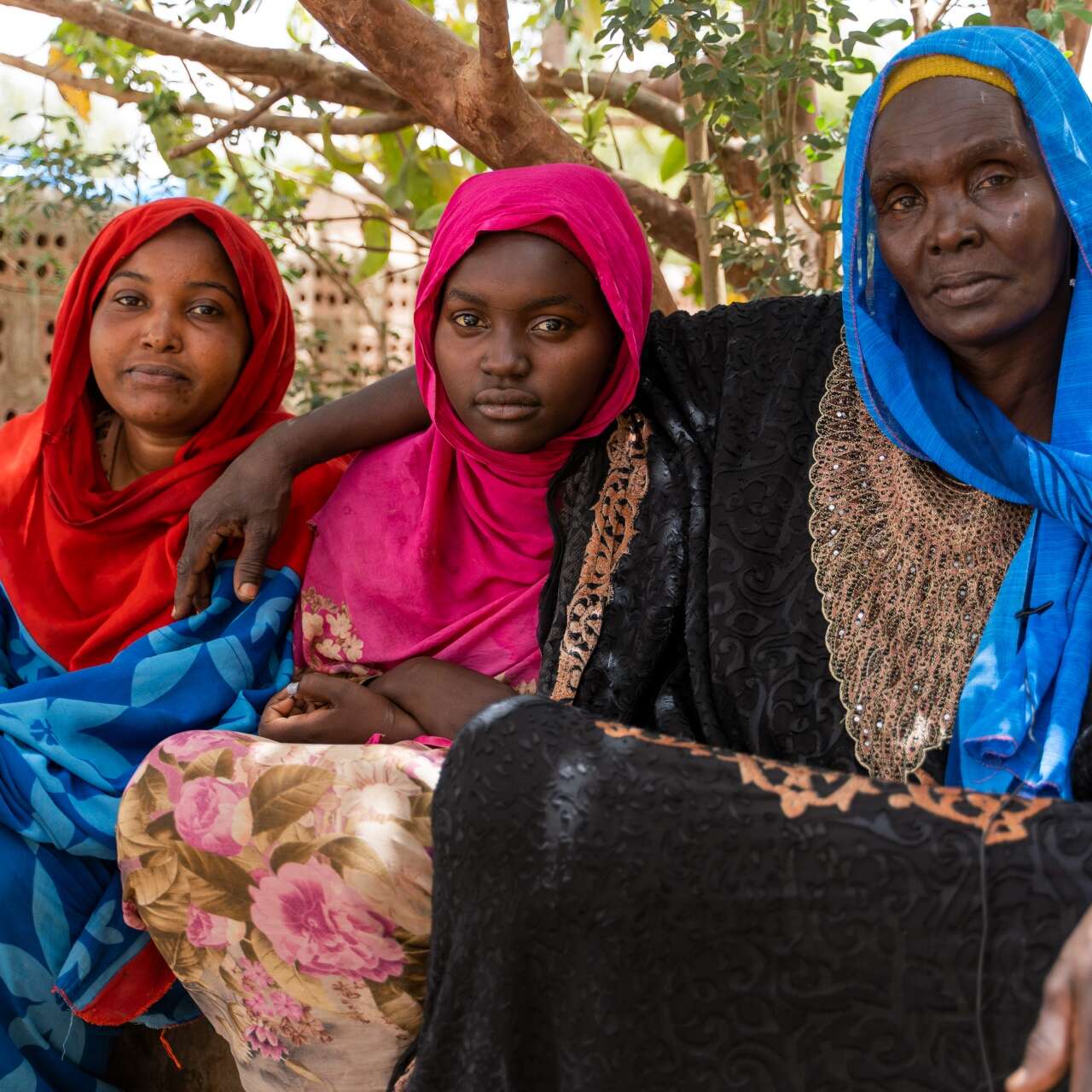 A mother and two daughters stare solemnly into the camera while posing for a portrait.