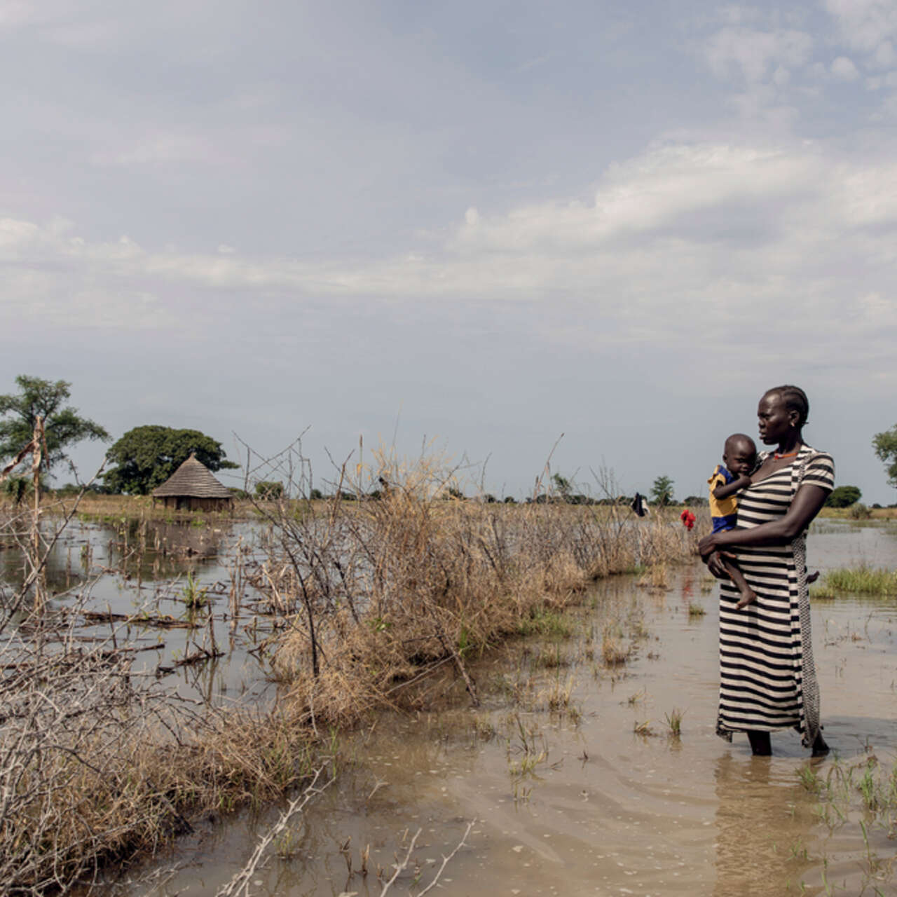 Abuk, holding Nyirou, poses for a portrait in front of their flooded house, in Northern Bahr El Ghazal, South Sudan.