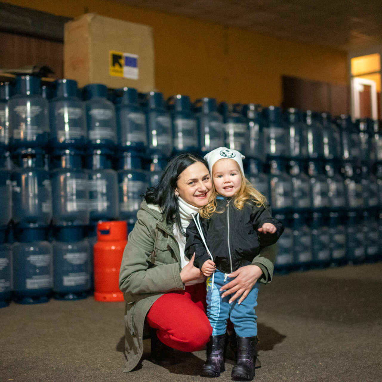 A mother and her small child in front of emergency supplies provided by the IRC and EU