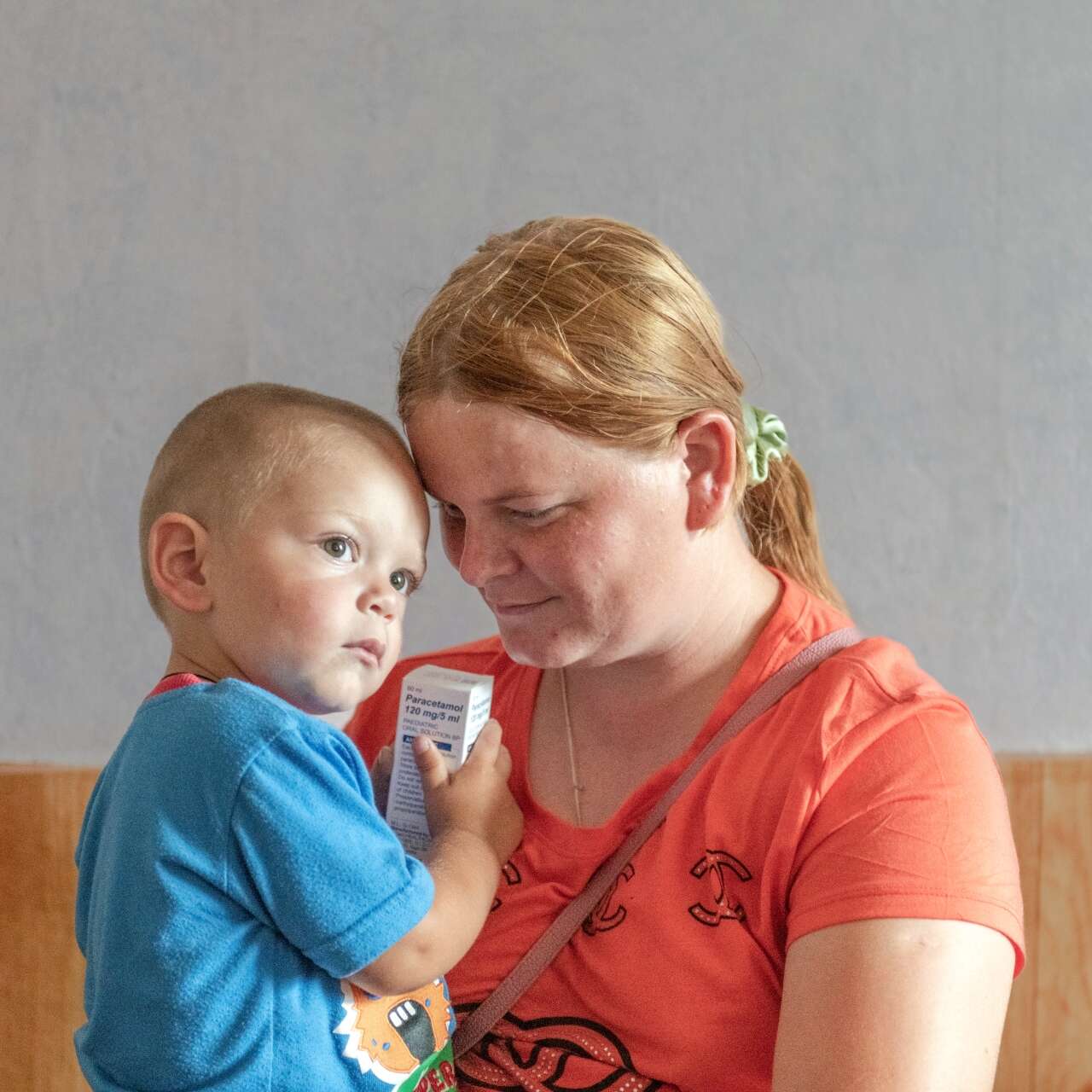 A mother holds her young son in her arms, looking down and smiling at him.