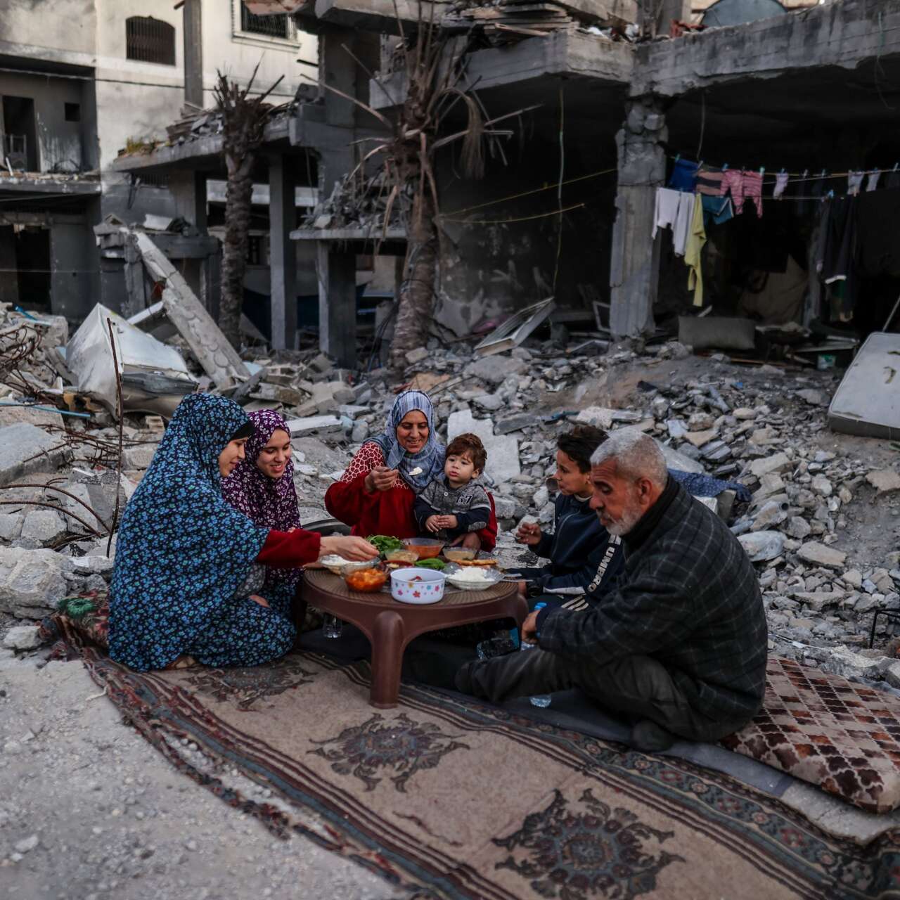 Eine Familie sitzt zusammen inmitten von Trümmern und teilt ihre iftar Mahlzeit während des Ramadan.