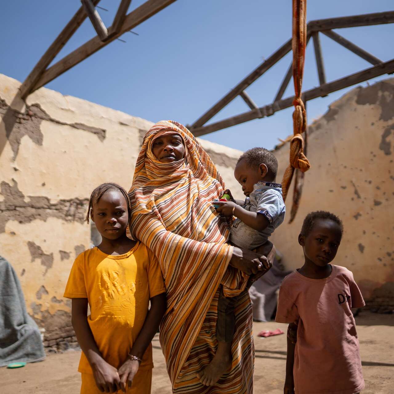 March 26, 2024 - Gedaref, Sudan. Altuma (45), and her children stand inside their roofless shelter.