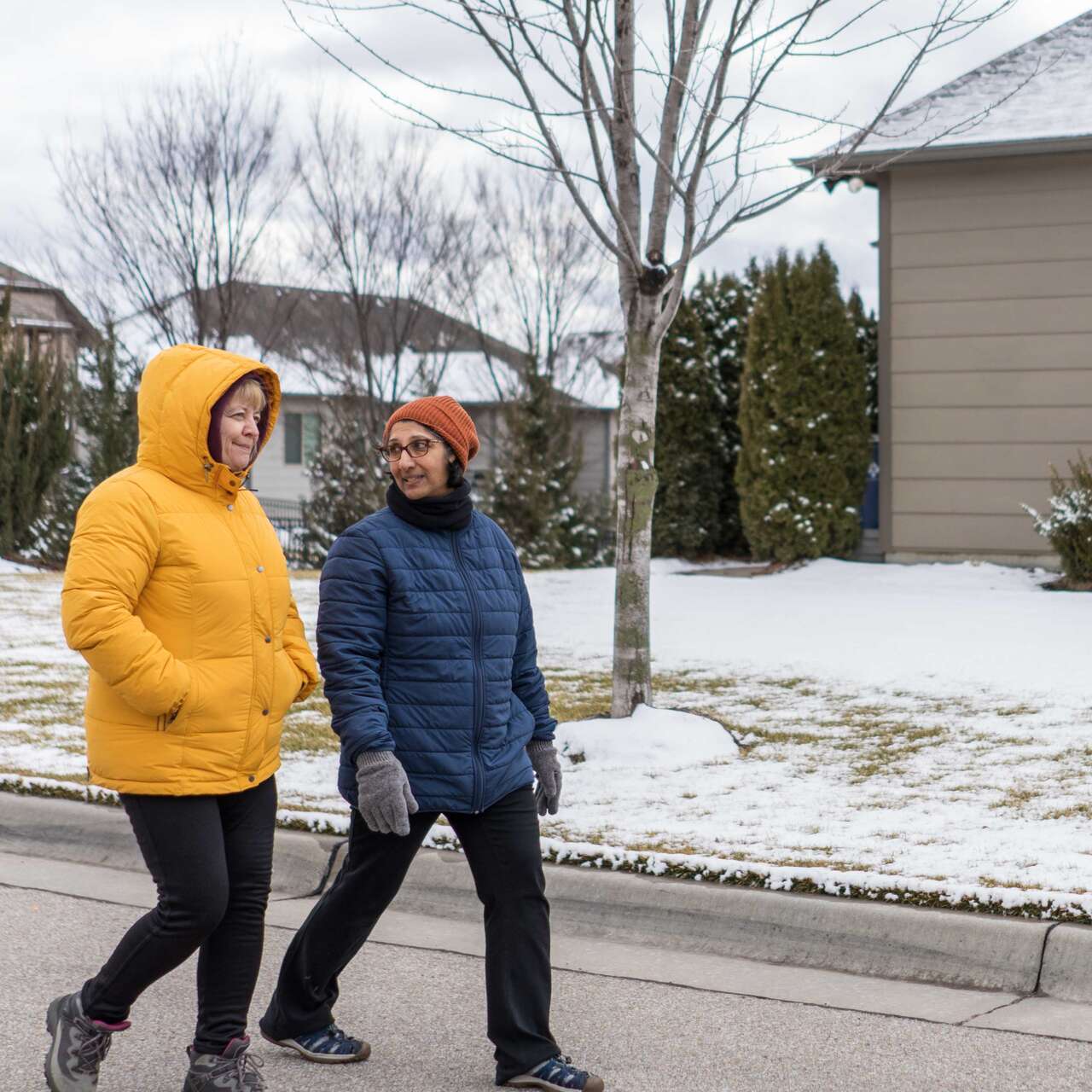 Two women walk together through a residential neighborhood in winter.