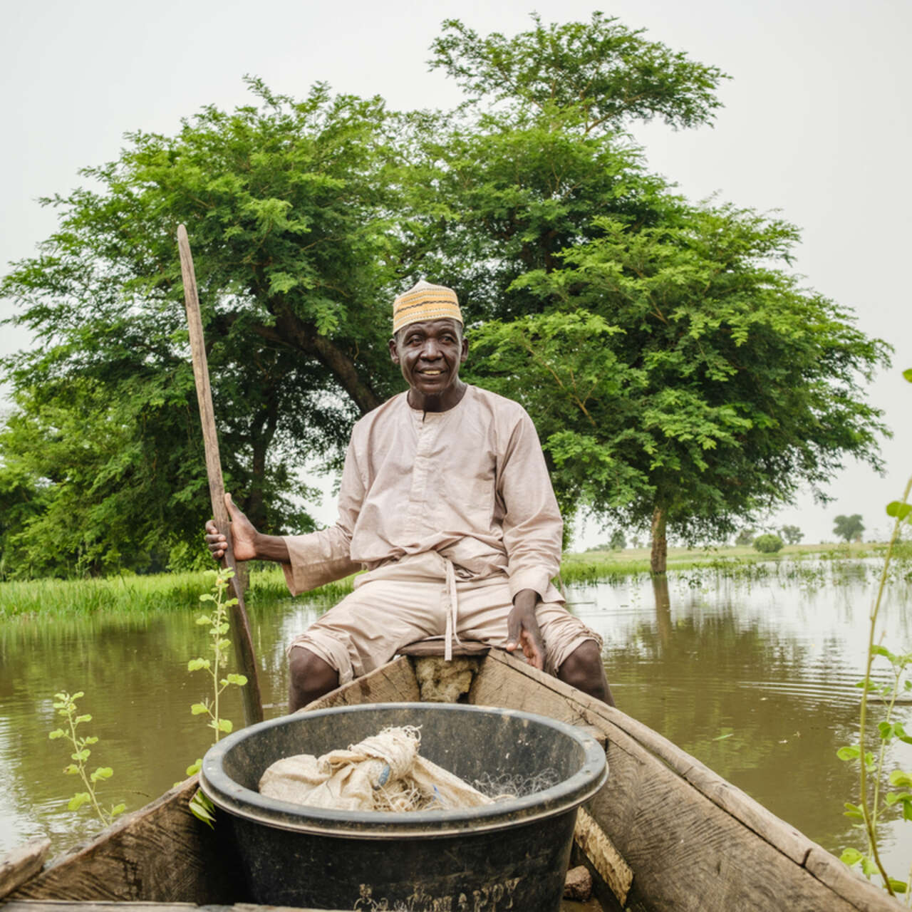 En fiskare sitter i en båt omgiven av ett grönt landskap i Nigeria. 