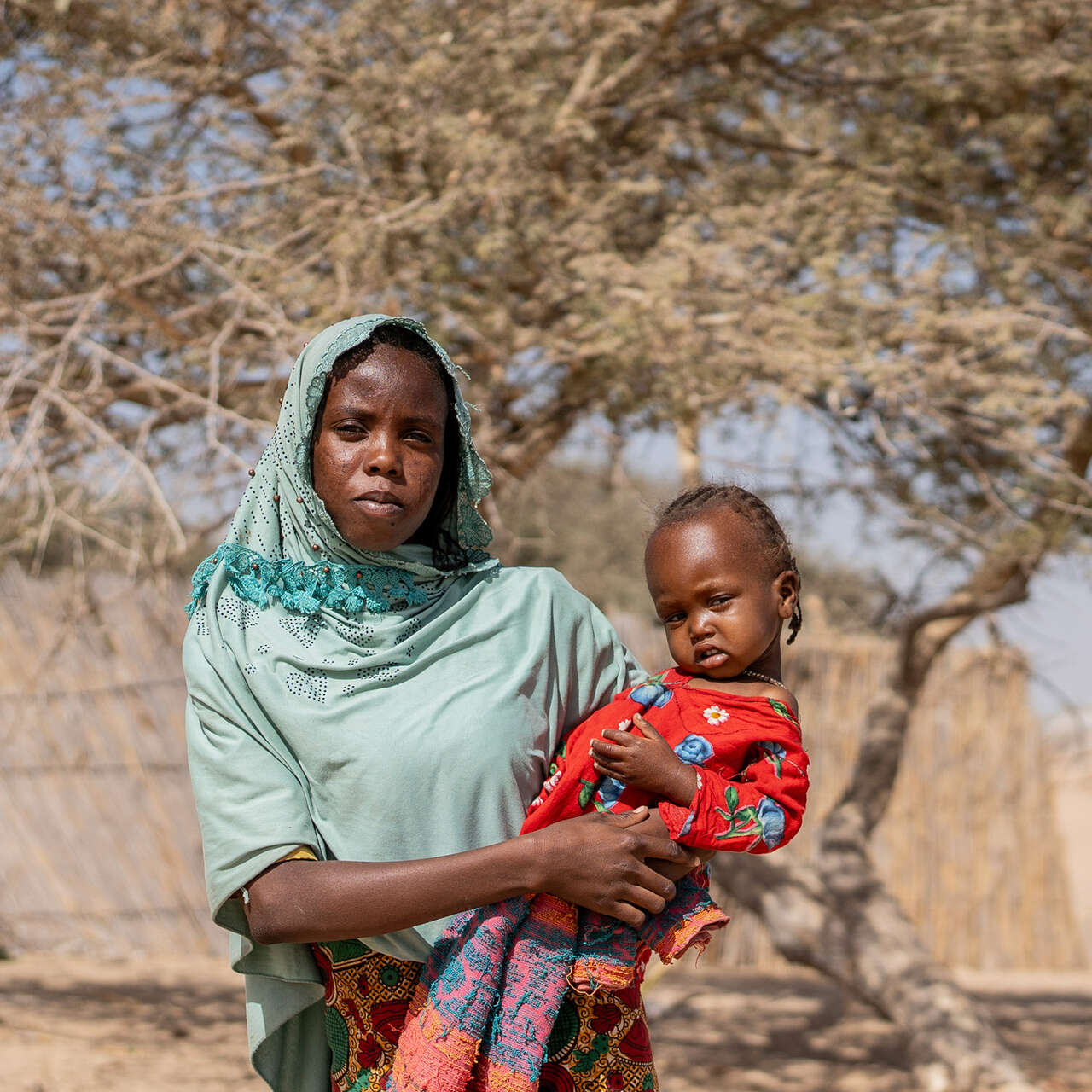 A mother holds her daughter and the pair poses for a photo outside of a home in Chad.