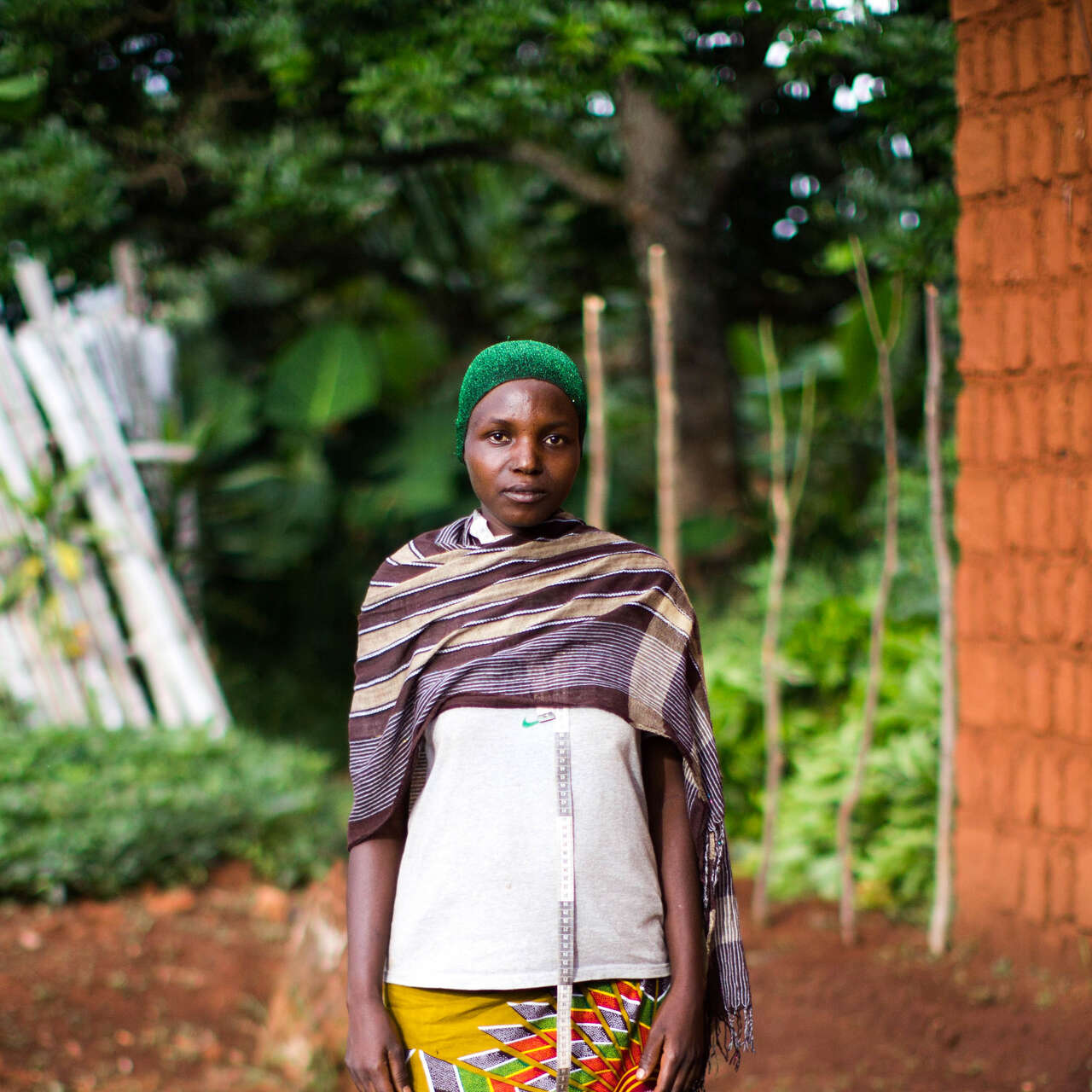 Eine Frau mit einem grünen Hut posiert für ein Foto vor einem Haus in Burundi.