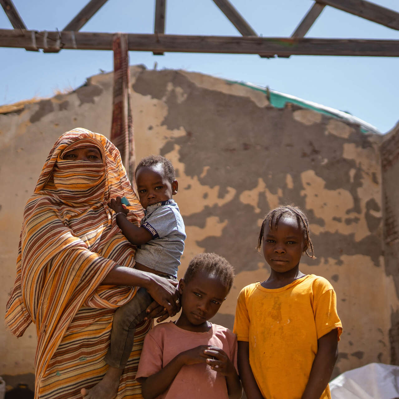 A mother stands with her three children in the ruins of a destroyed building in Sudan.