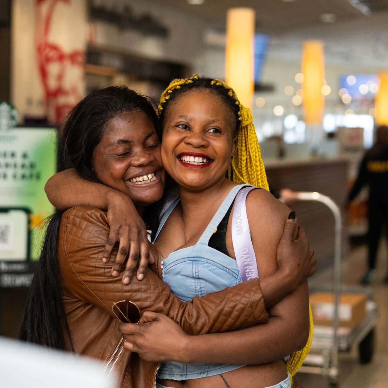 Two women stand and embrace after reunifying at an airport.