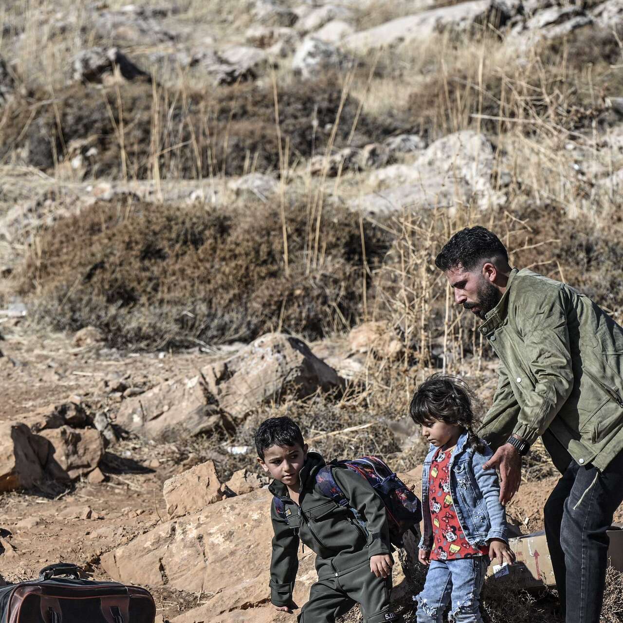 A family walks through an arid landscape with their belongings.