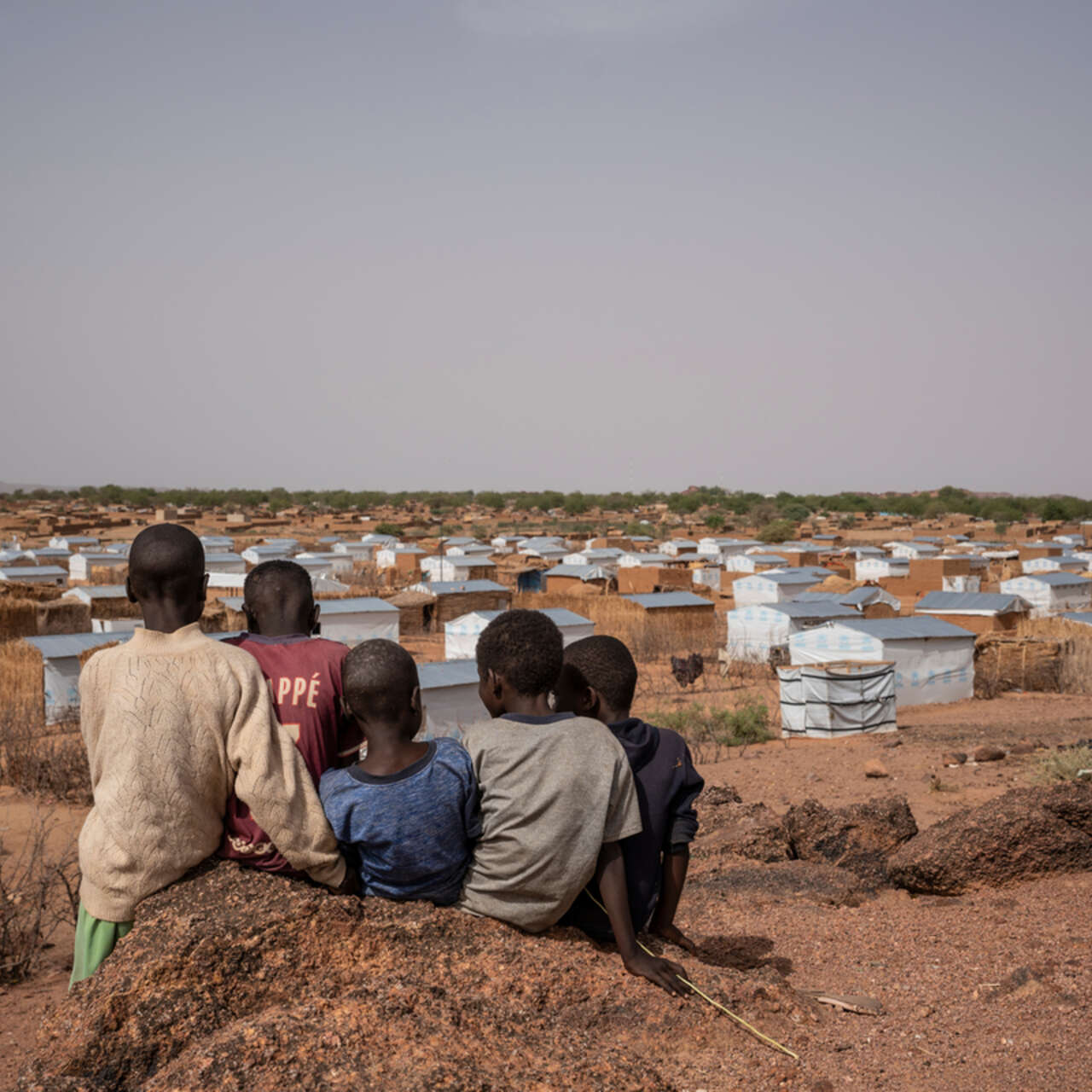 Barn sitter på en kulle och tittar ut mot ett flyktingläger i Tchad