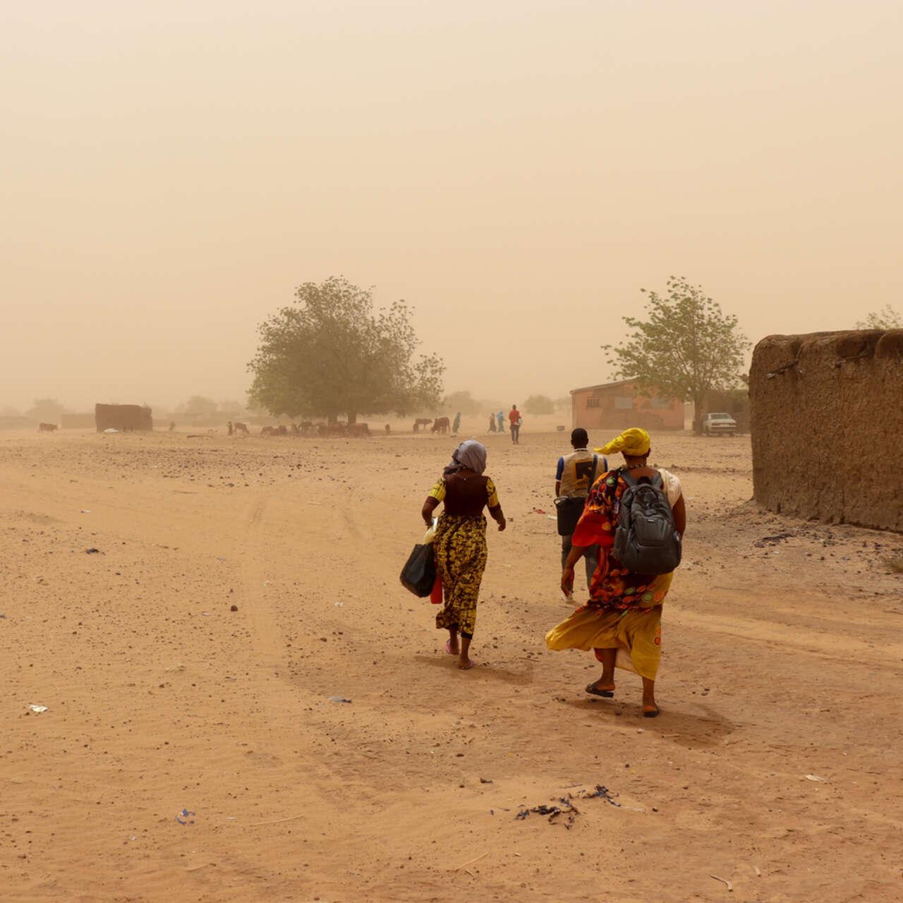 Tre personer i Mali går i kraftig vind och sand yr omkring dem. 