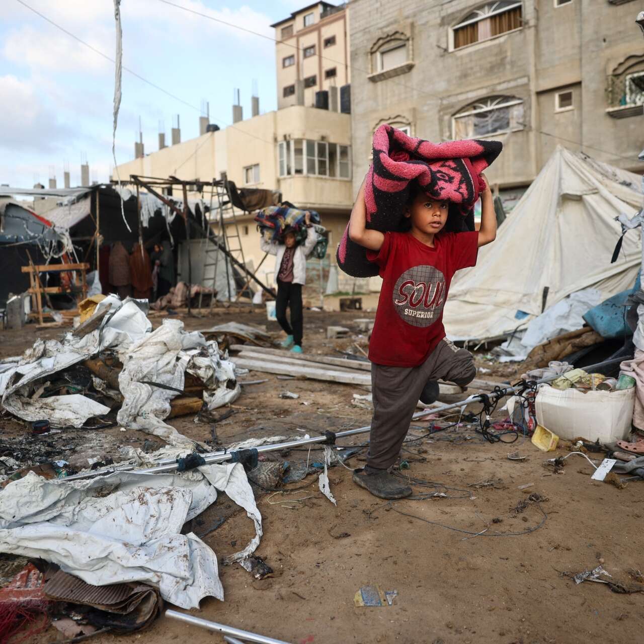 A boy carries a blanket through a destroyed neighborhood in Gaza.