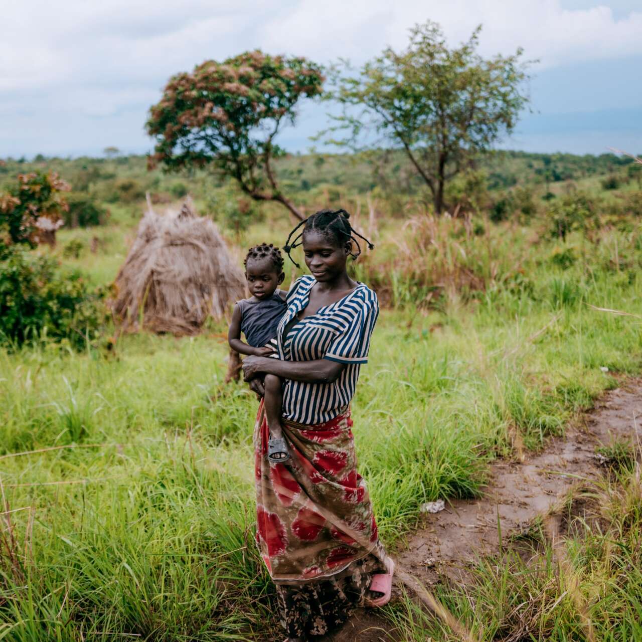 A mother walks through a field while holding her child in her arm.