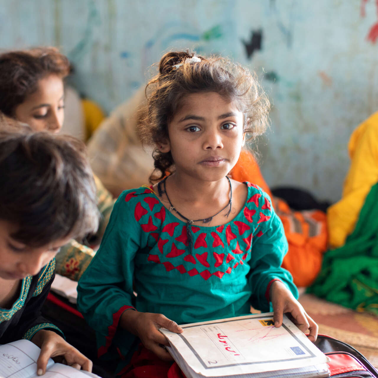 En flicka i Pakistan sitter i ett klassrum och tittar in i kameran.