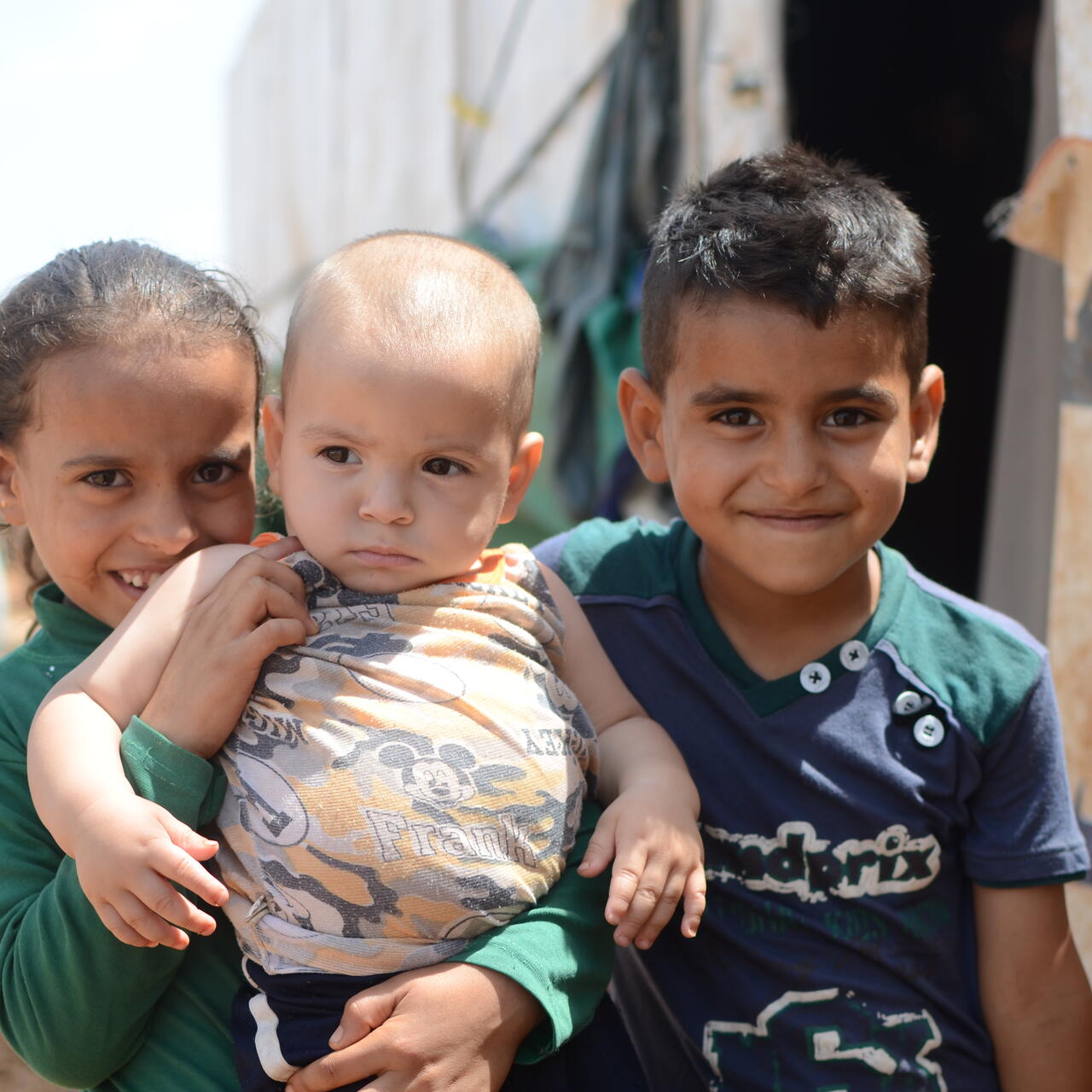 Two Syrian children hold a baby outside a tent in a refugee settlement in Lebanon
