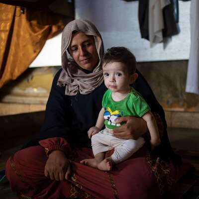 A Syrian mother holds her infant son, sitting on the ground where they live in an informal refugee settlement in Lebanon.