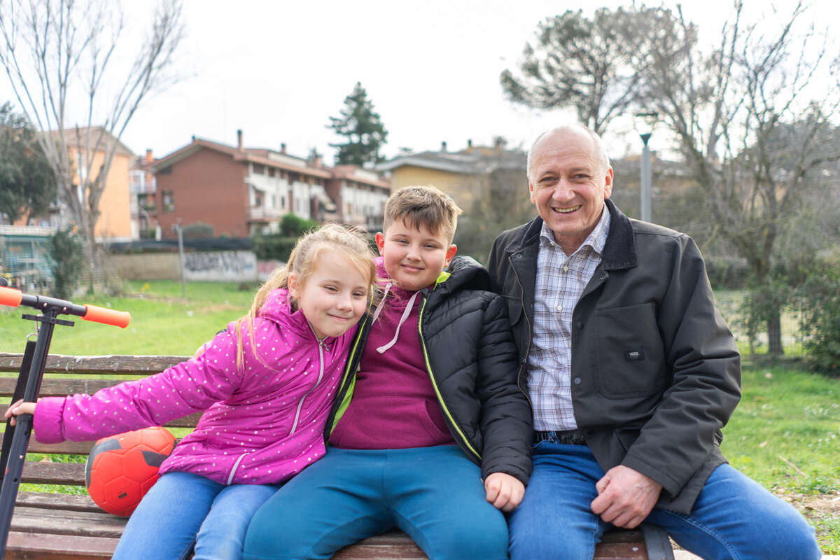 Oleksandr sits on a bench with his two grandchildren.