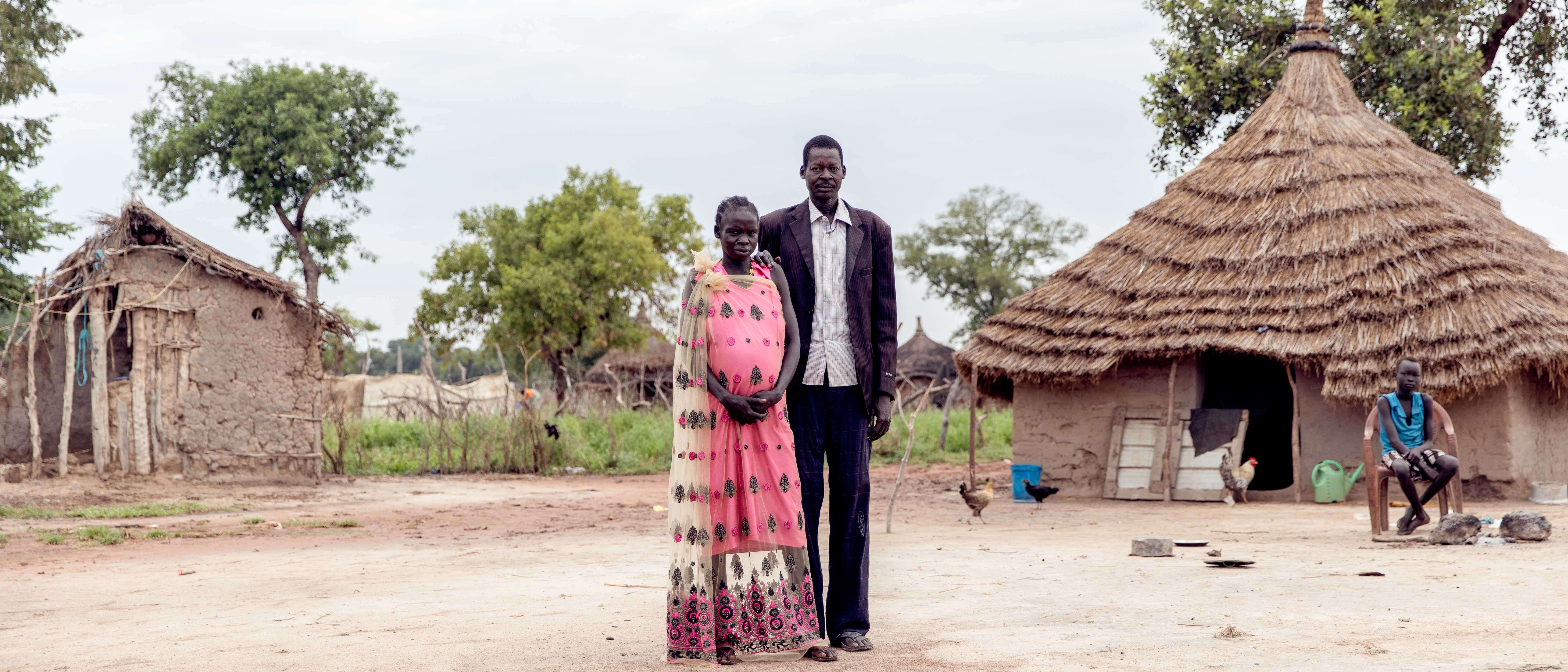 A man and woman embrace while posing for a photo outside their home in South Sudan.