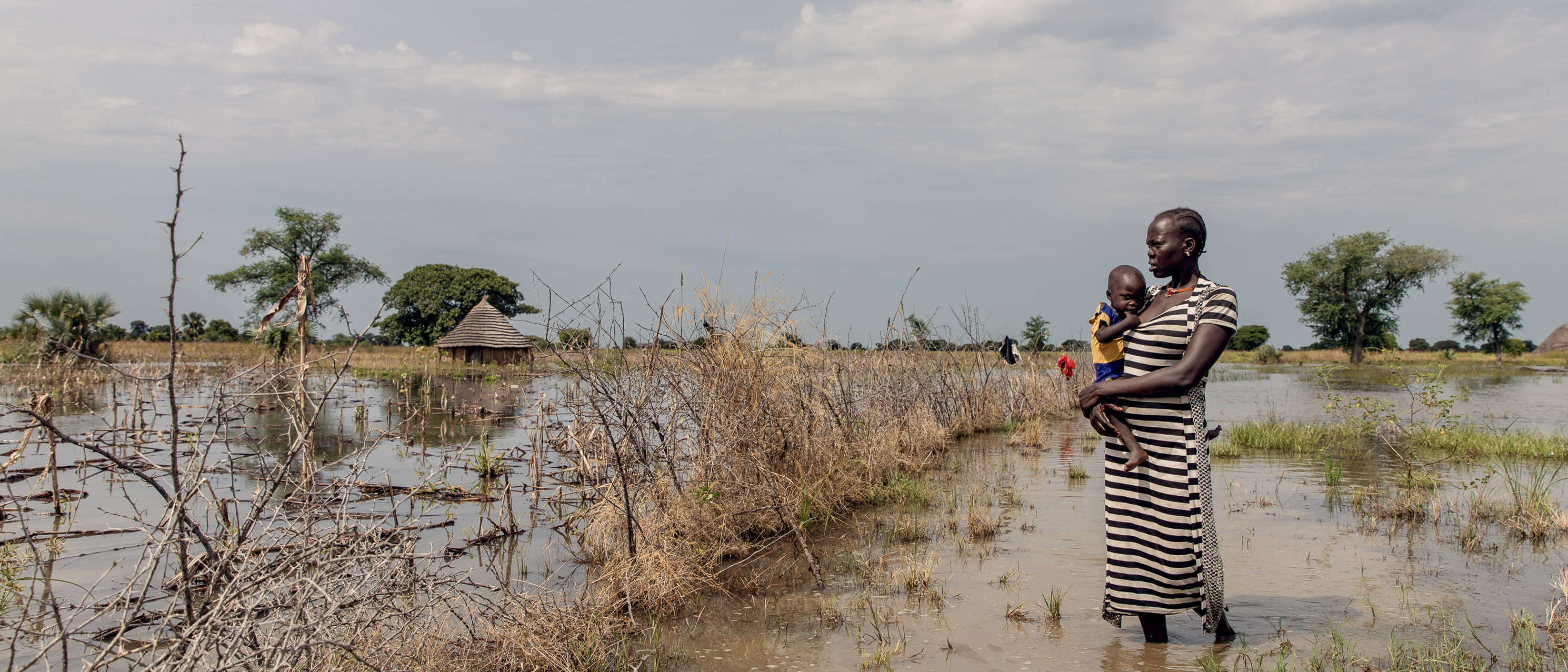 A mother holds her daughter tight to her chest while walking outdoors in a flooded region of South Sudan.