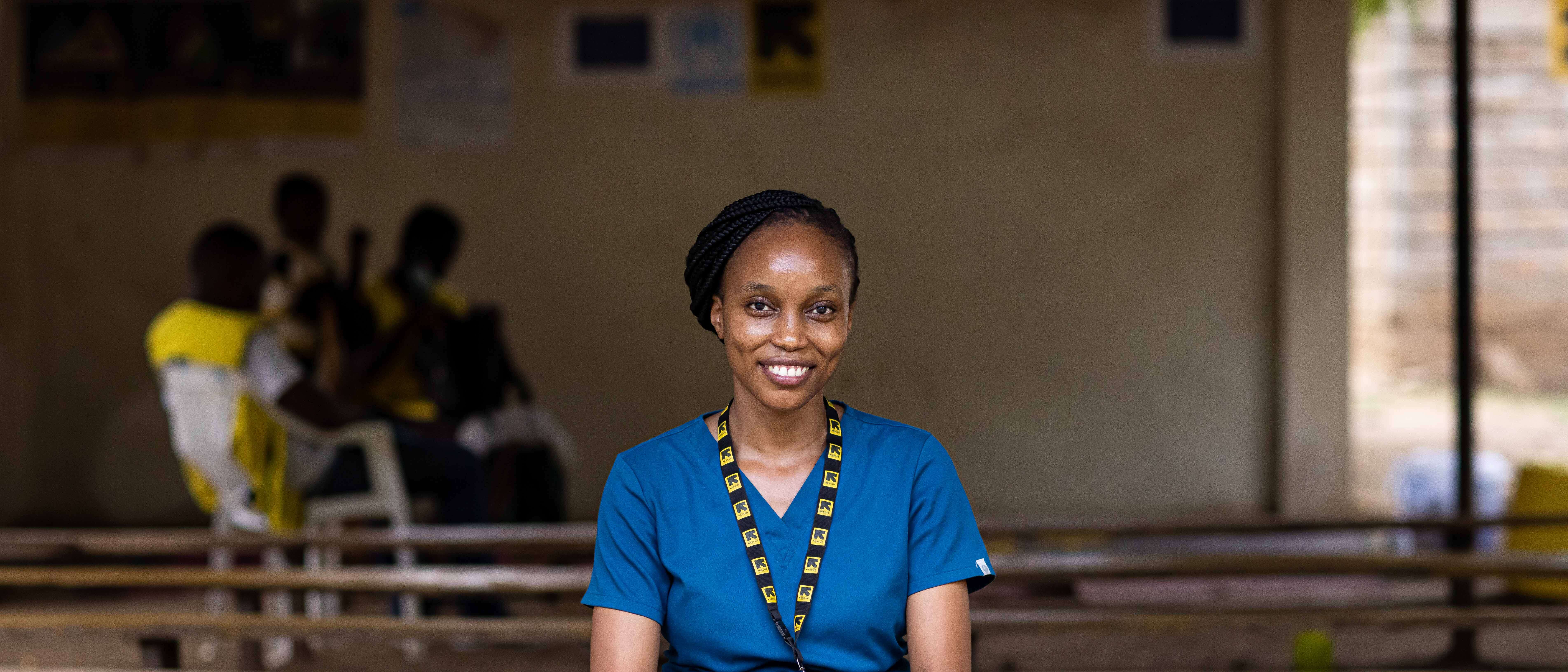 A woman wearing blue nurses scrub and an IRC lanyard, smiles and poses for a photo.