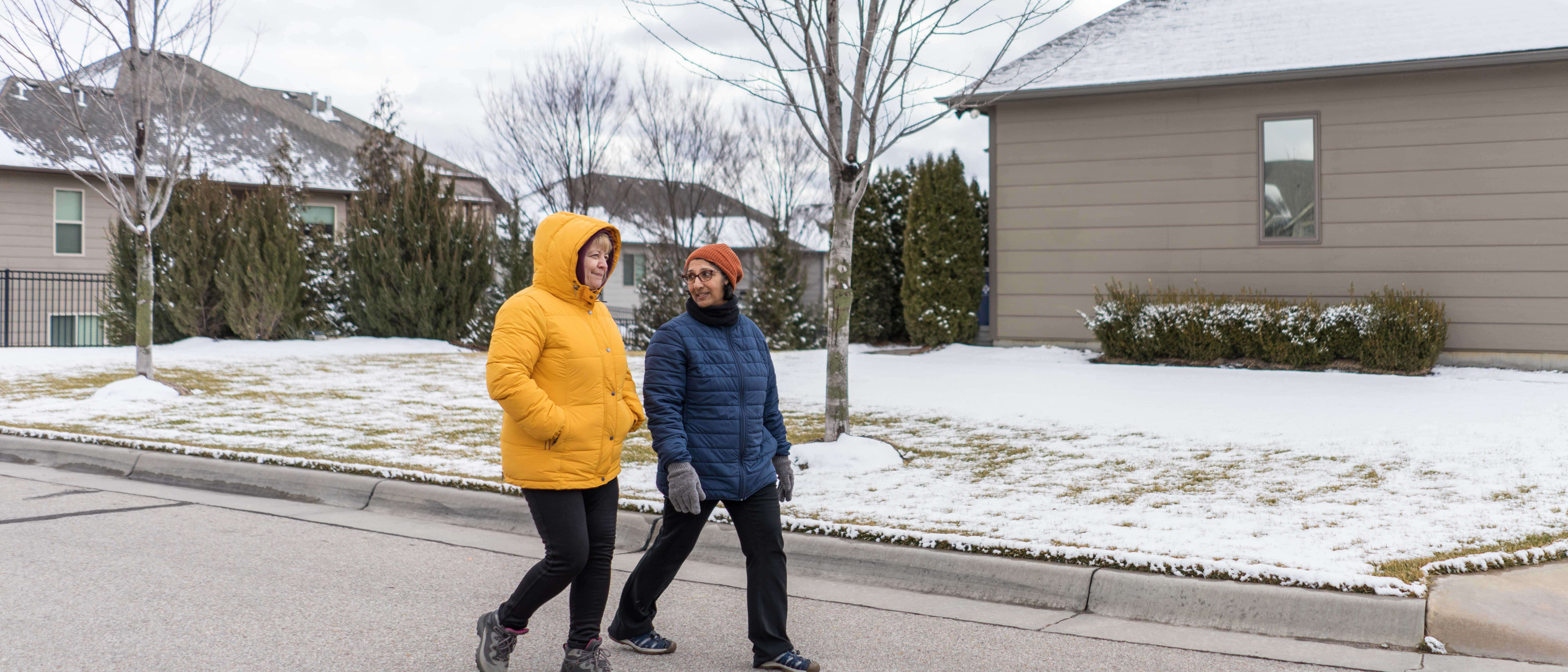 Two women walk together through a residential neighborhood in winter.