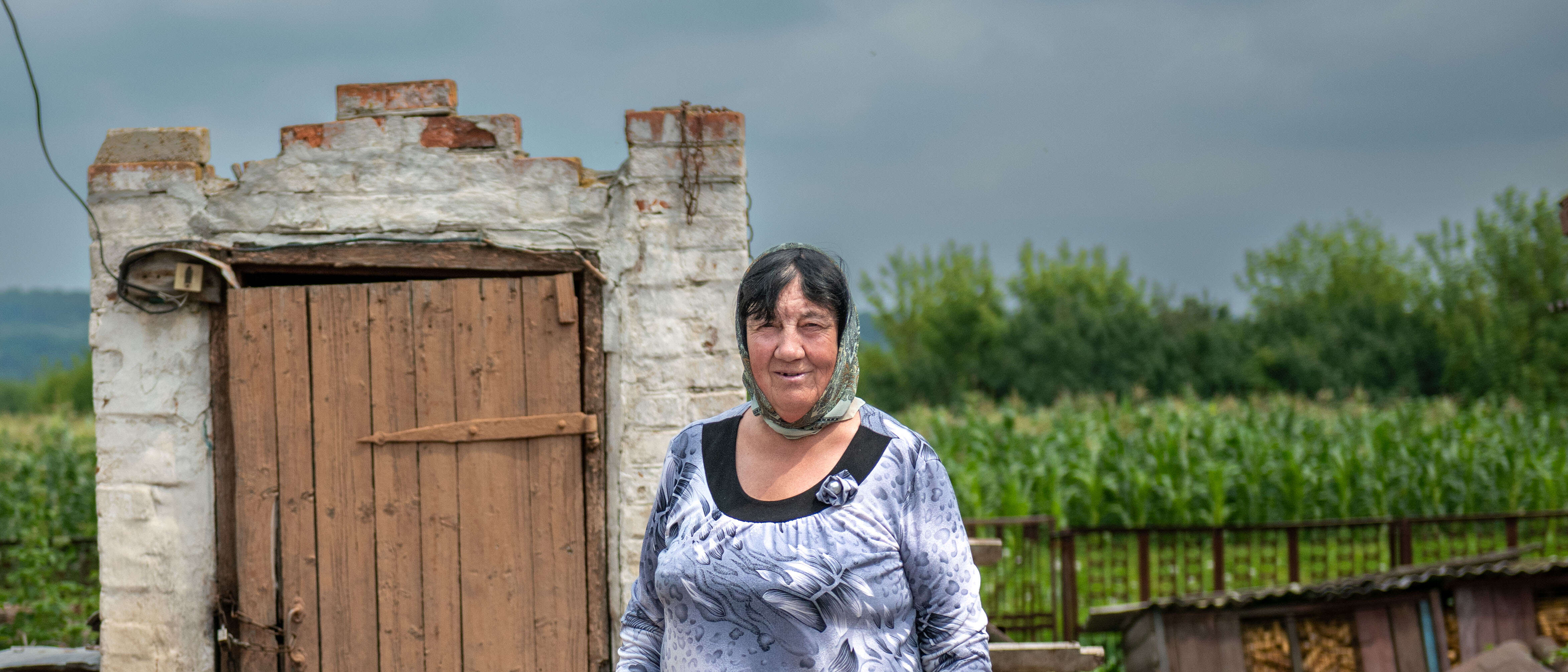 A woman poses for a photo in front of a building destroyed by the war in Ukraine.