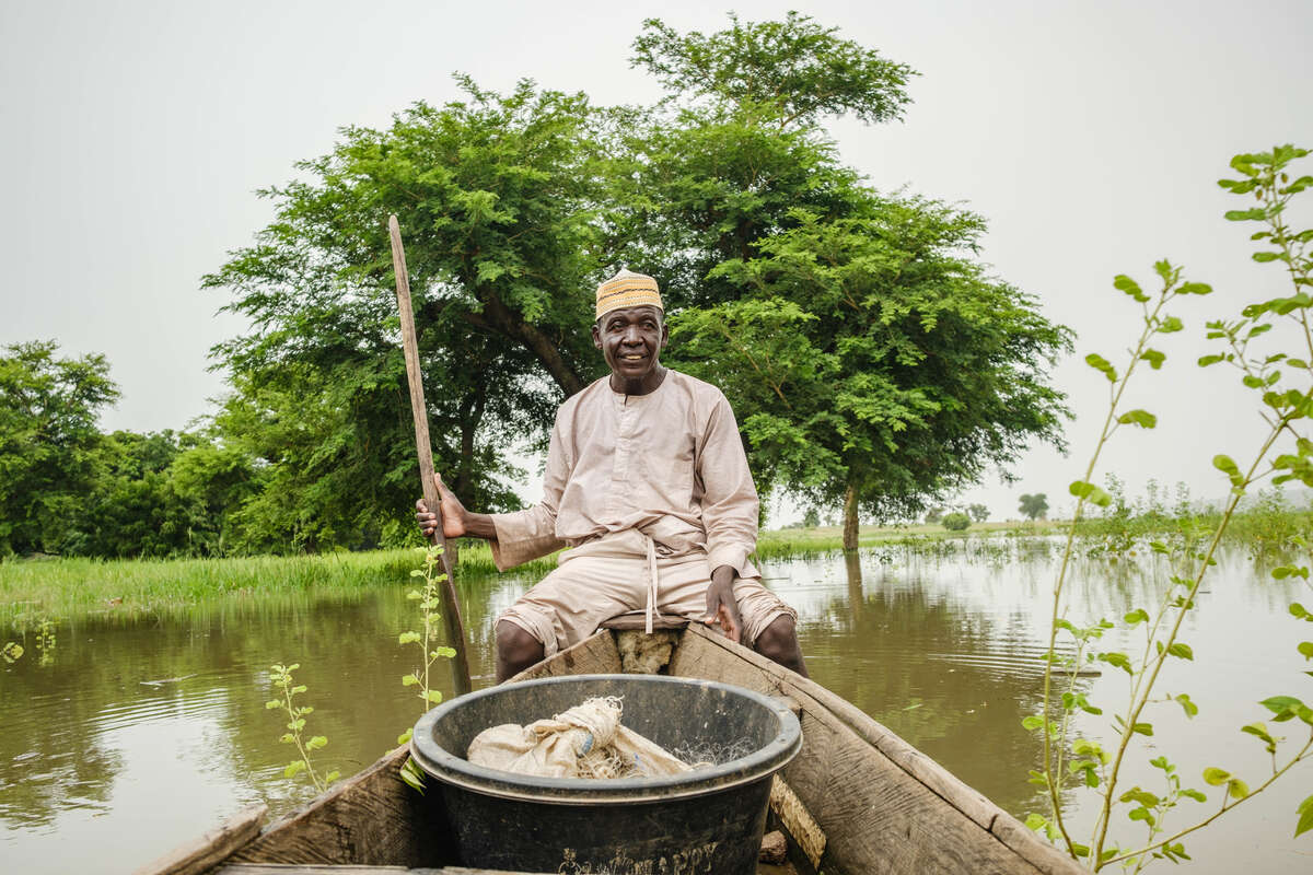 En fiskare sitter i en båt omgiven av ett grönt landskap i Nigeria. 