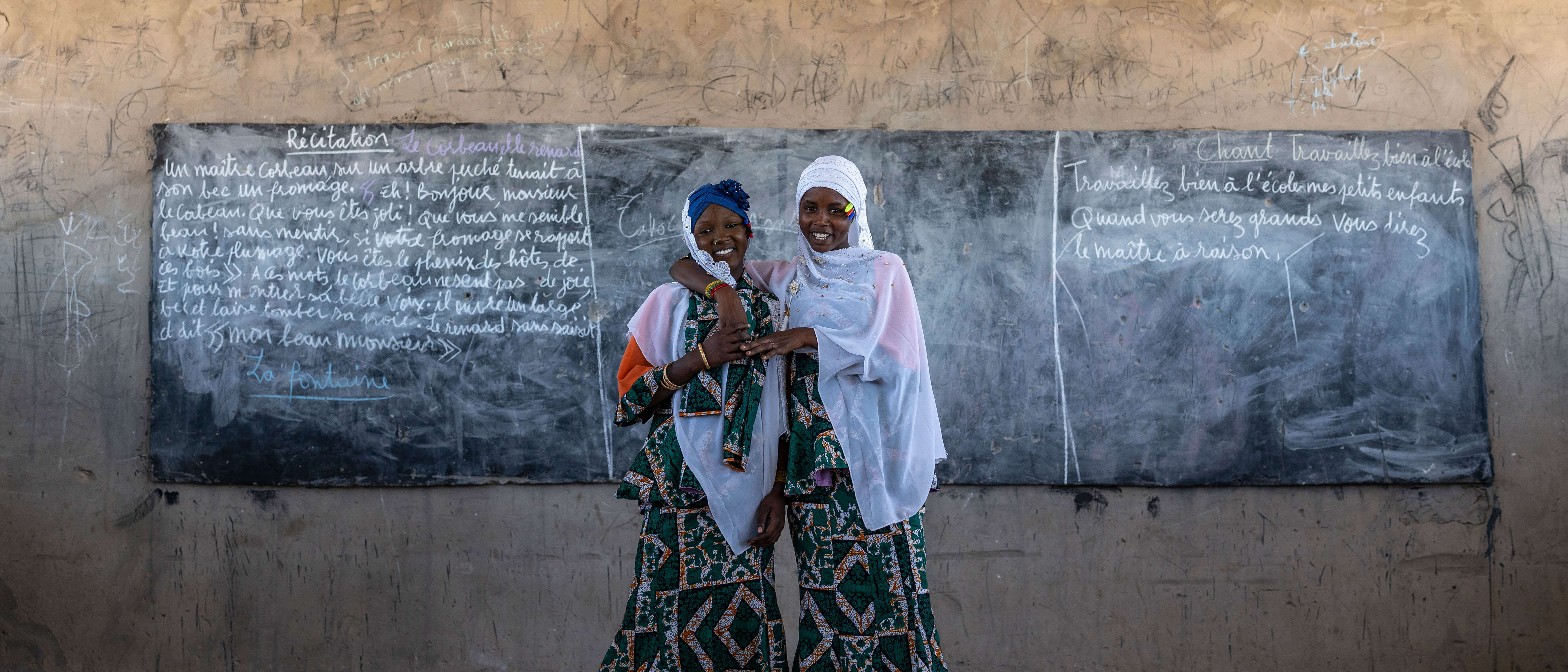 Two women embrace each other and share a smile while posing in a school in Chad.