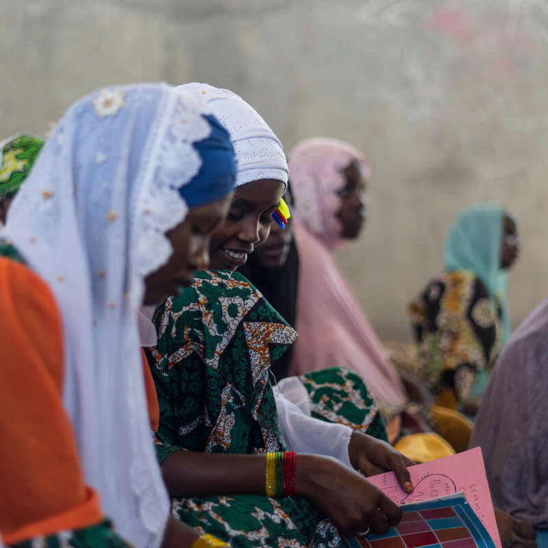 Flera flickor i en skolsal i Chad sitter på en skolbänk, en bläddrar i en bok.